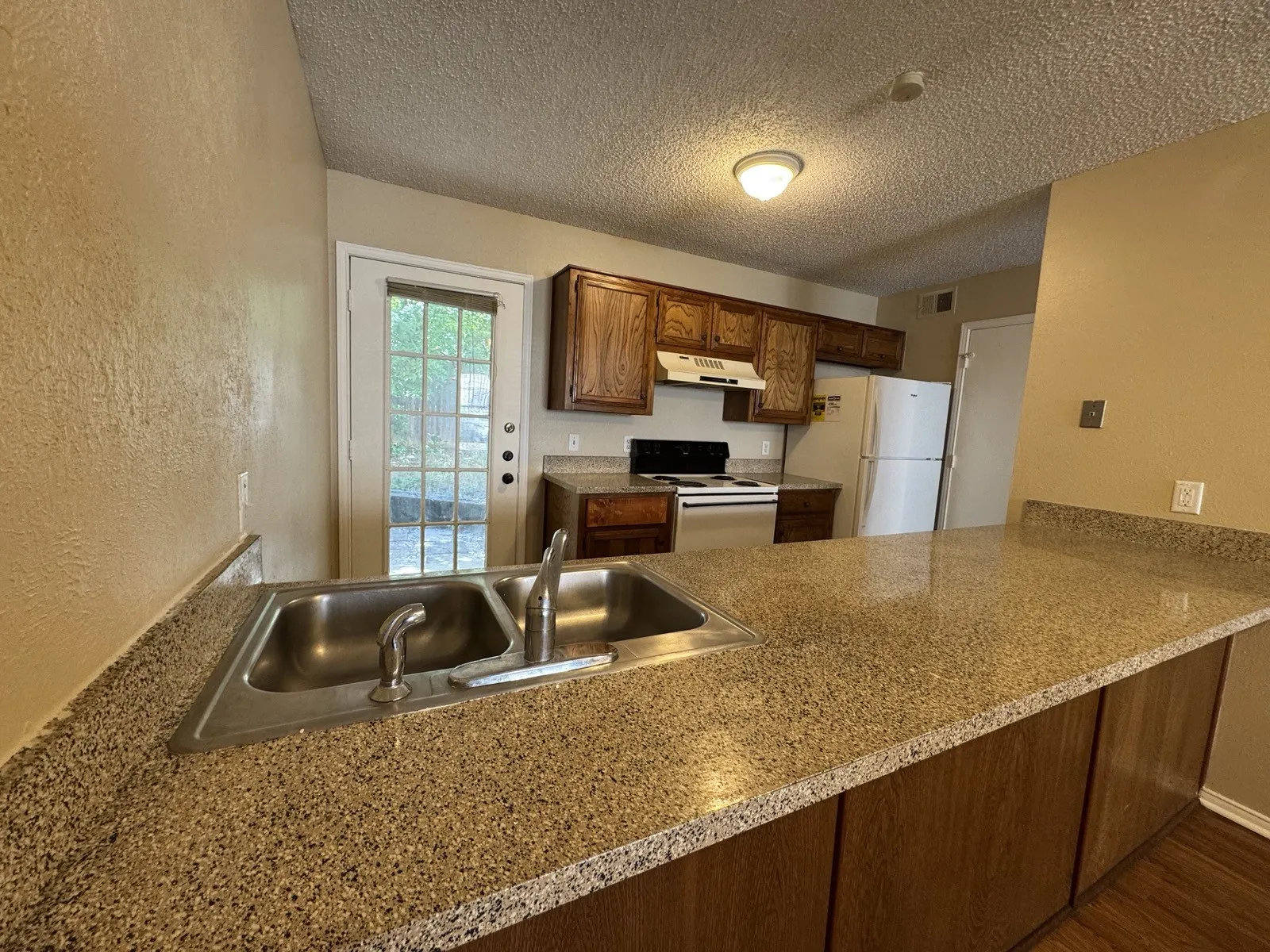 Kitchen featuring granite-look countertops, a double basin stainless steel sink, wood cabinetry, and a glass-paned door