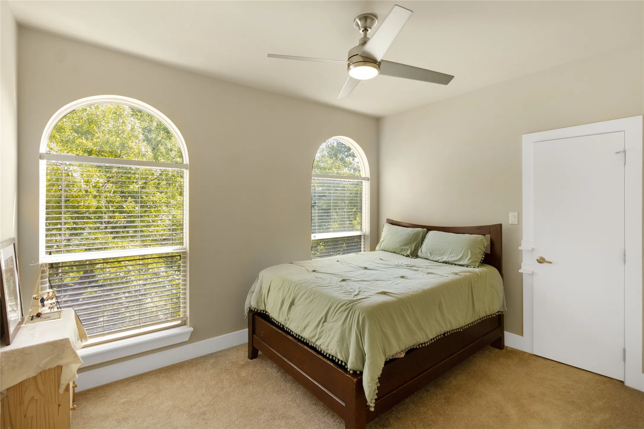 This room features two arched windows with blinds, neutral wall paint, and a contemporary ceiling fan with integrated lighting