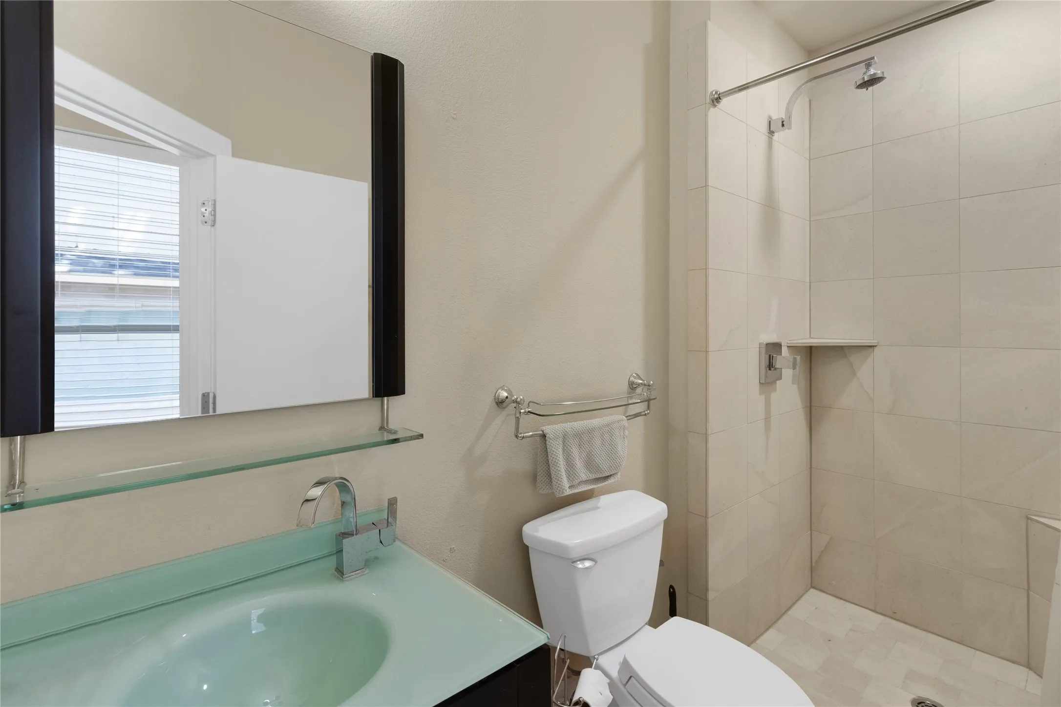 Bathroom featuring a glass sink, chrome fixtures, a modern mirror with a glass shelf, and a tiled shower with an integrated niche