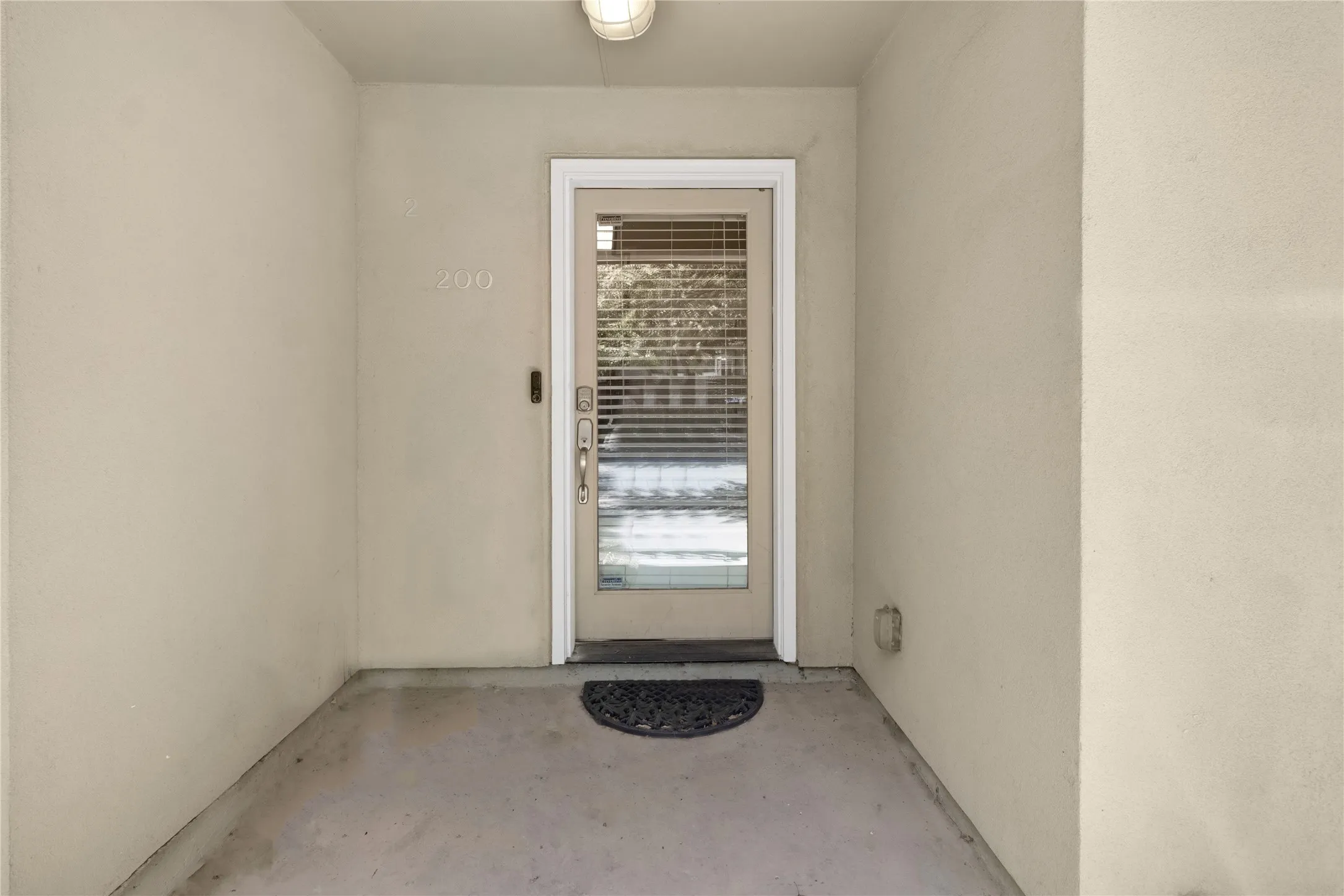 Covered porch entry featuring a glass panel door with integrated blinds, a contemporary wall sconce, and textured stucco walls