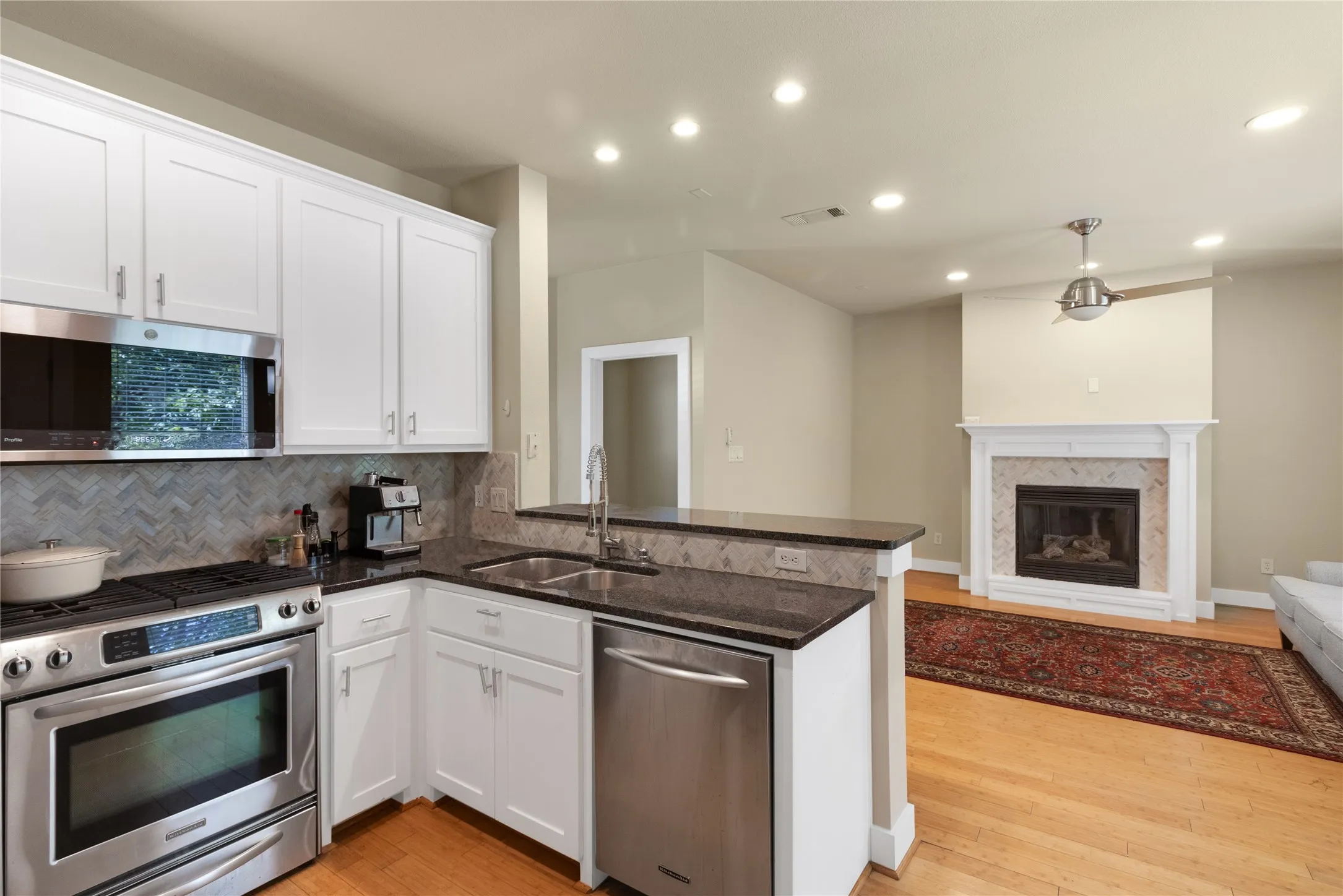 Well-appointed kitchen featuring white cabinetry, stainless steel appliances, dark countertops, and a tile backsplash