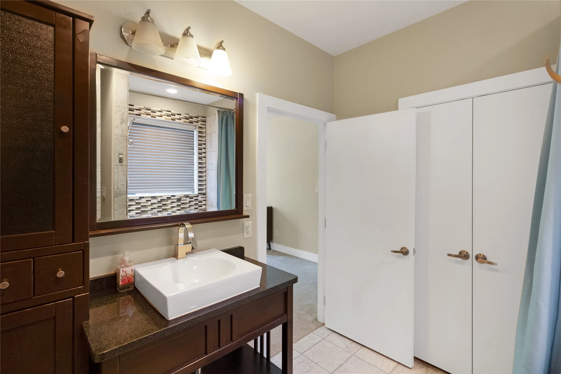 Bathroom featuring a vessel sink with a dark countertop, a framed mirror, a wall-mounted light fixture, and a dark wood storage cabinet