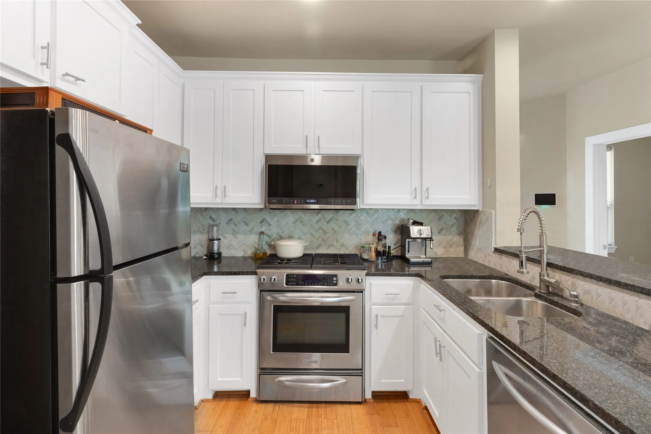Well-appointed kitchen featuring white cabinetry, stainless steel appliances, granite countertops, a herringbone tile backsplash, and wood-finish flooring