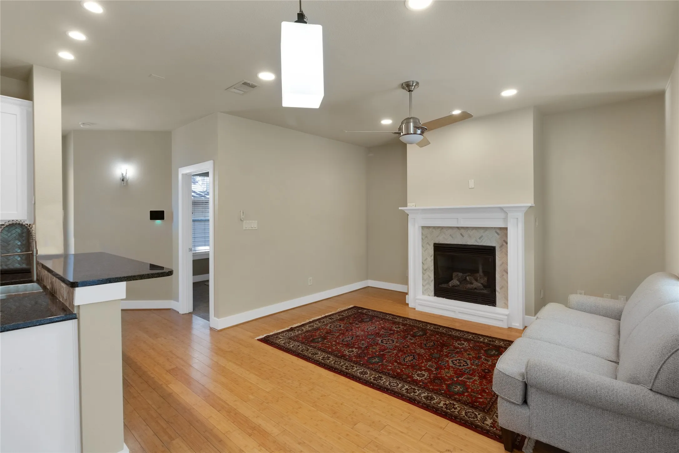 Living area featuring wood-finish flooring, a fireplace with a white mantel and tiled surround, recessed lighting, and a ceiling fan