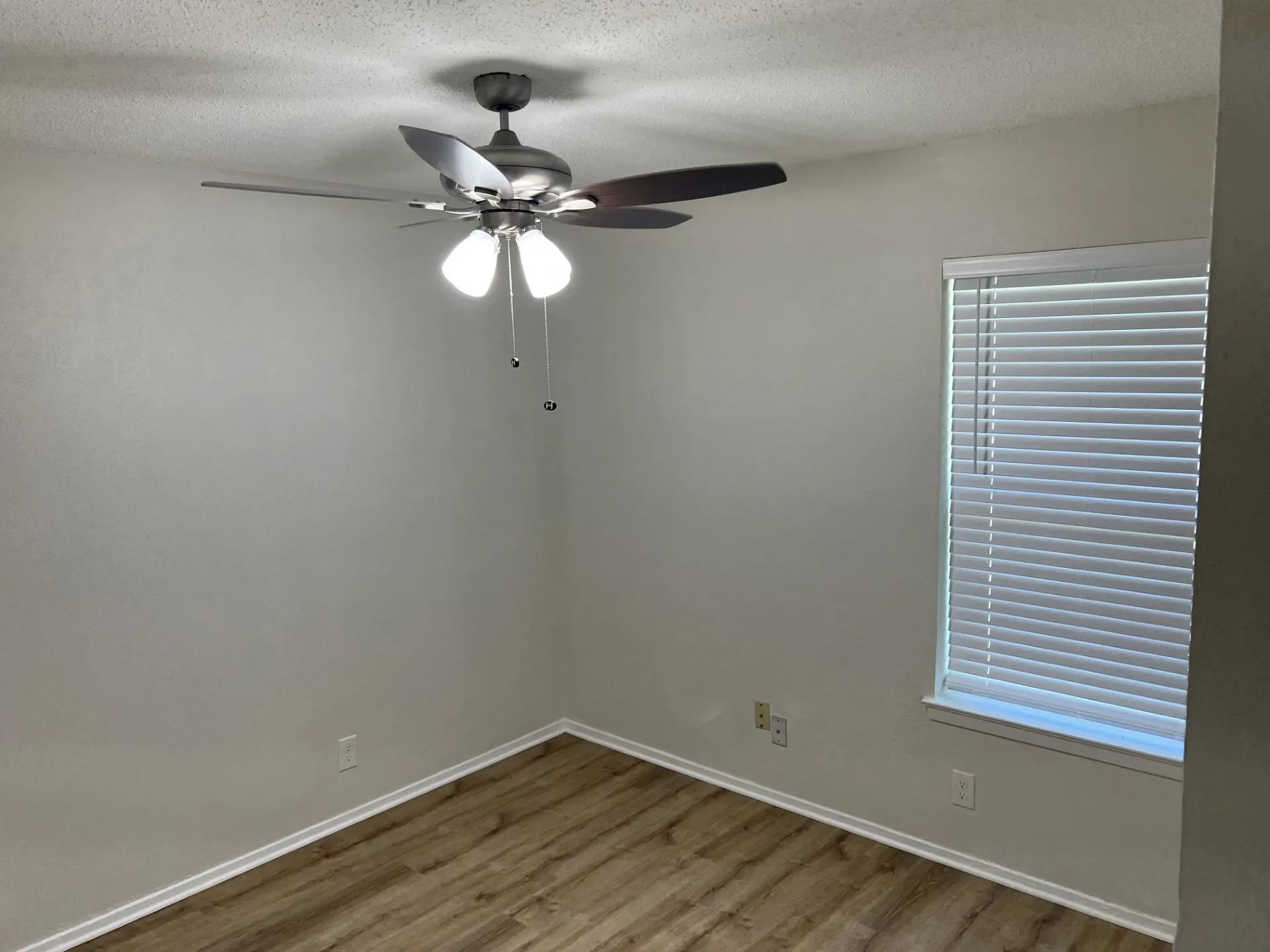 Interior space featuring wood-finish flooring, a ceiling fan with integrated lighting, and a window with horizontal blinds