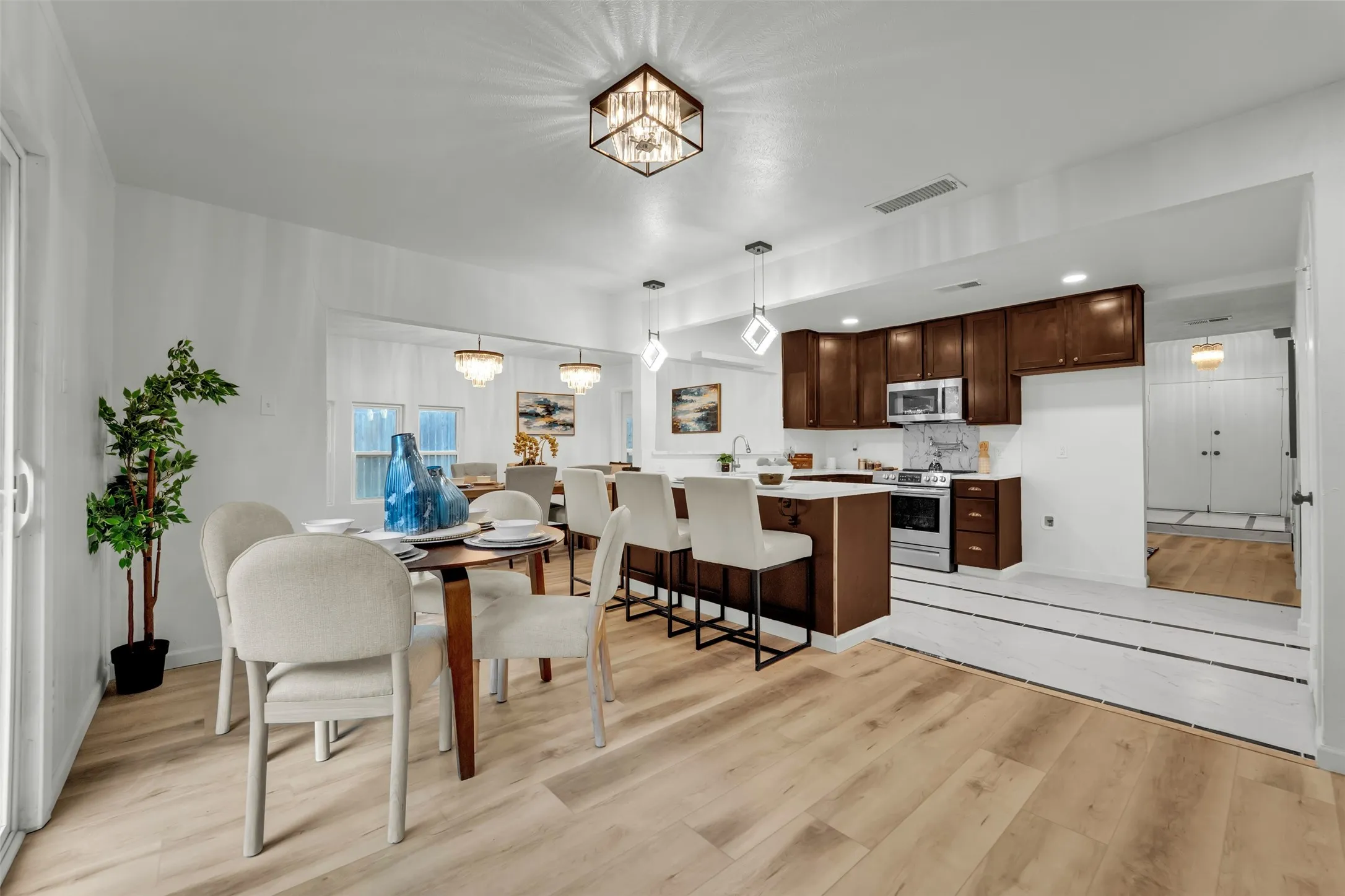 Open-concept living space featuring wood-finish flooring, a contemporary kitchen with dark wood cabinetry, white countertops, and stainless steel appliances