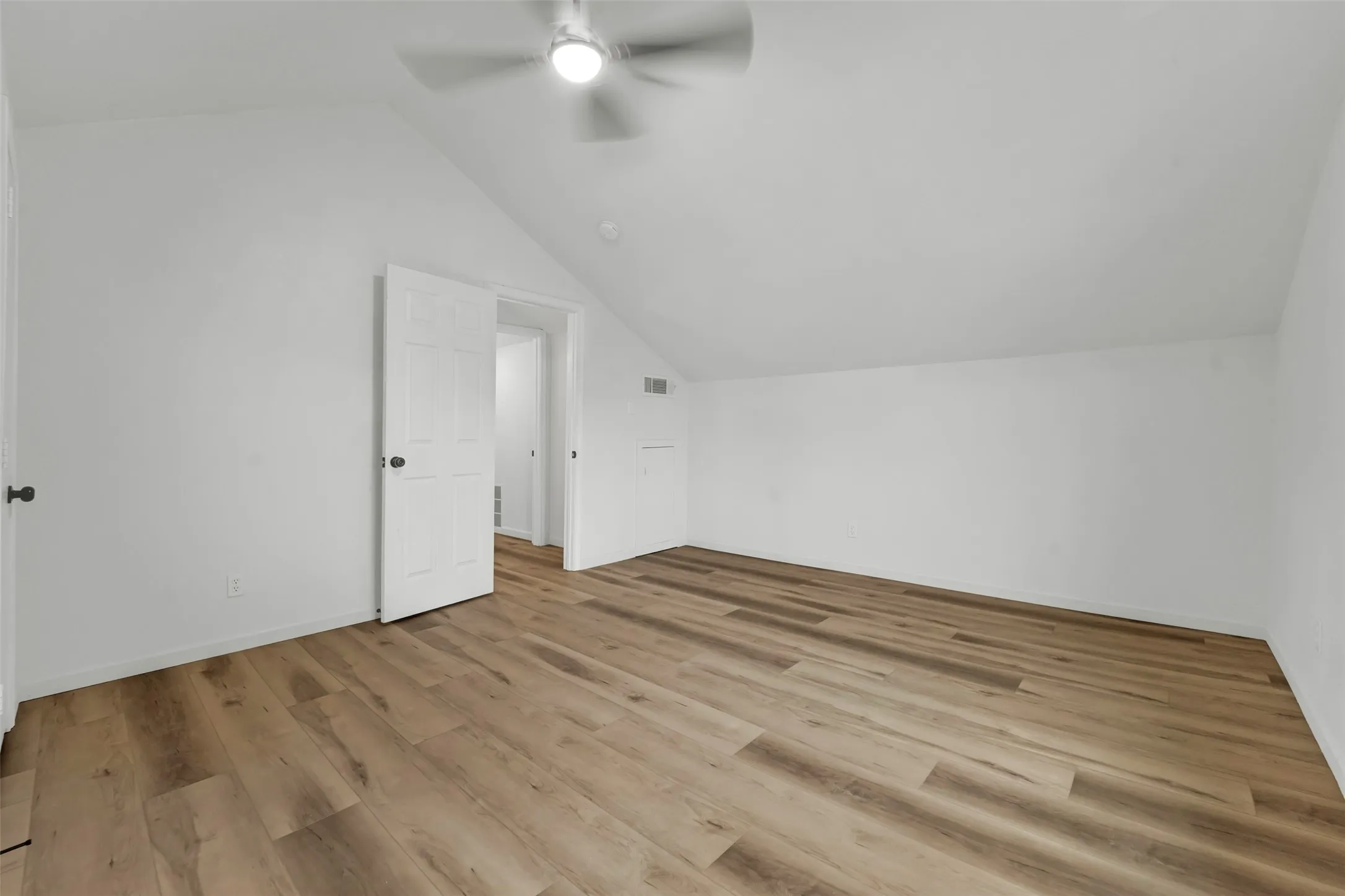 Spacious room featuring wood-finish flooring, a vaulted ceiling, and a ceiling fan with integrated lighting