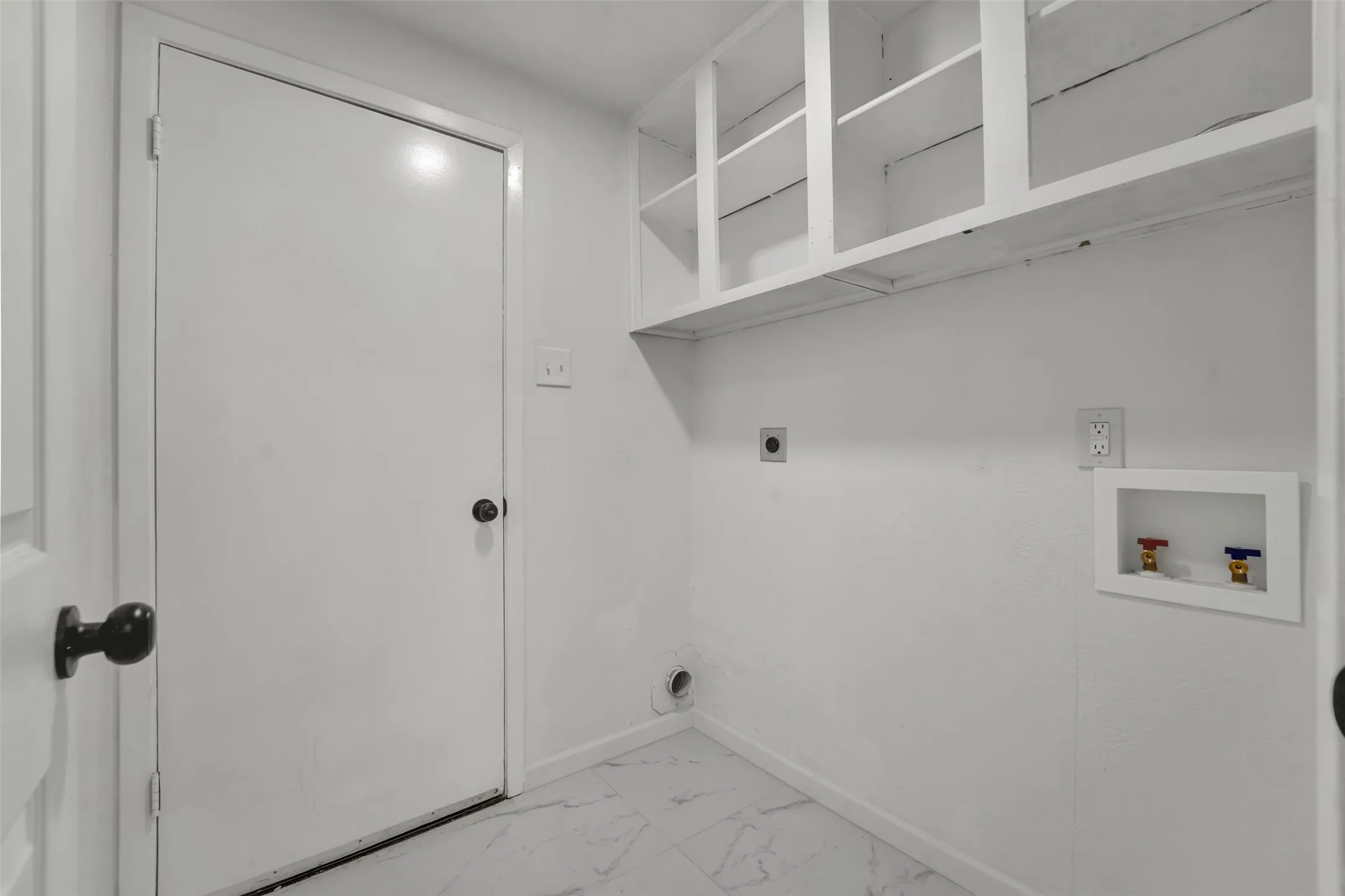 Laundry area featuring white walls, open shelving, and a patterned tile floor