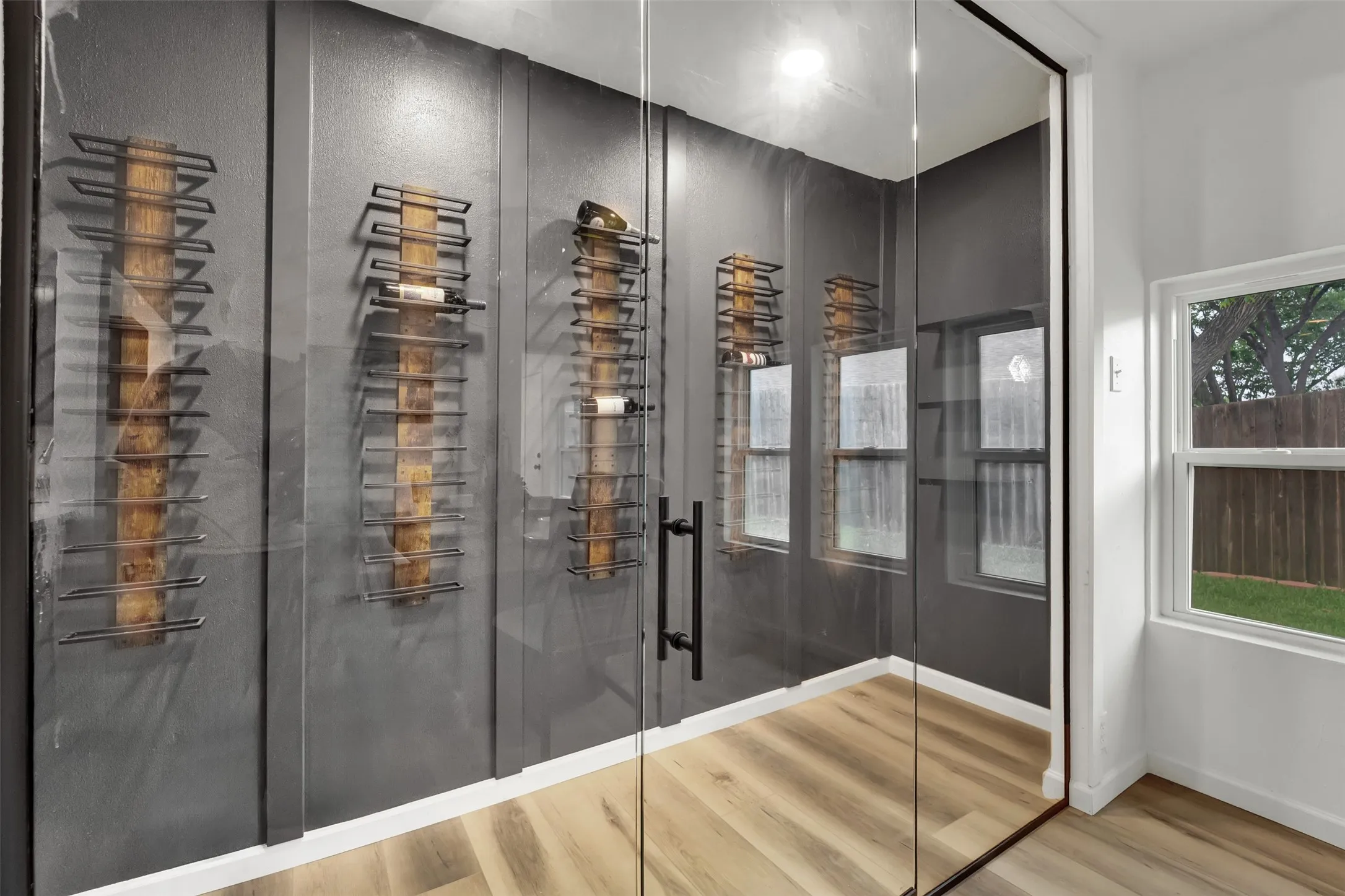 Dedicated wine room featuring a full glass entry, dark accent walls, built-in shelving, and wood-finish flooring