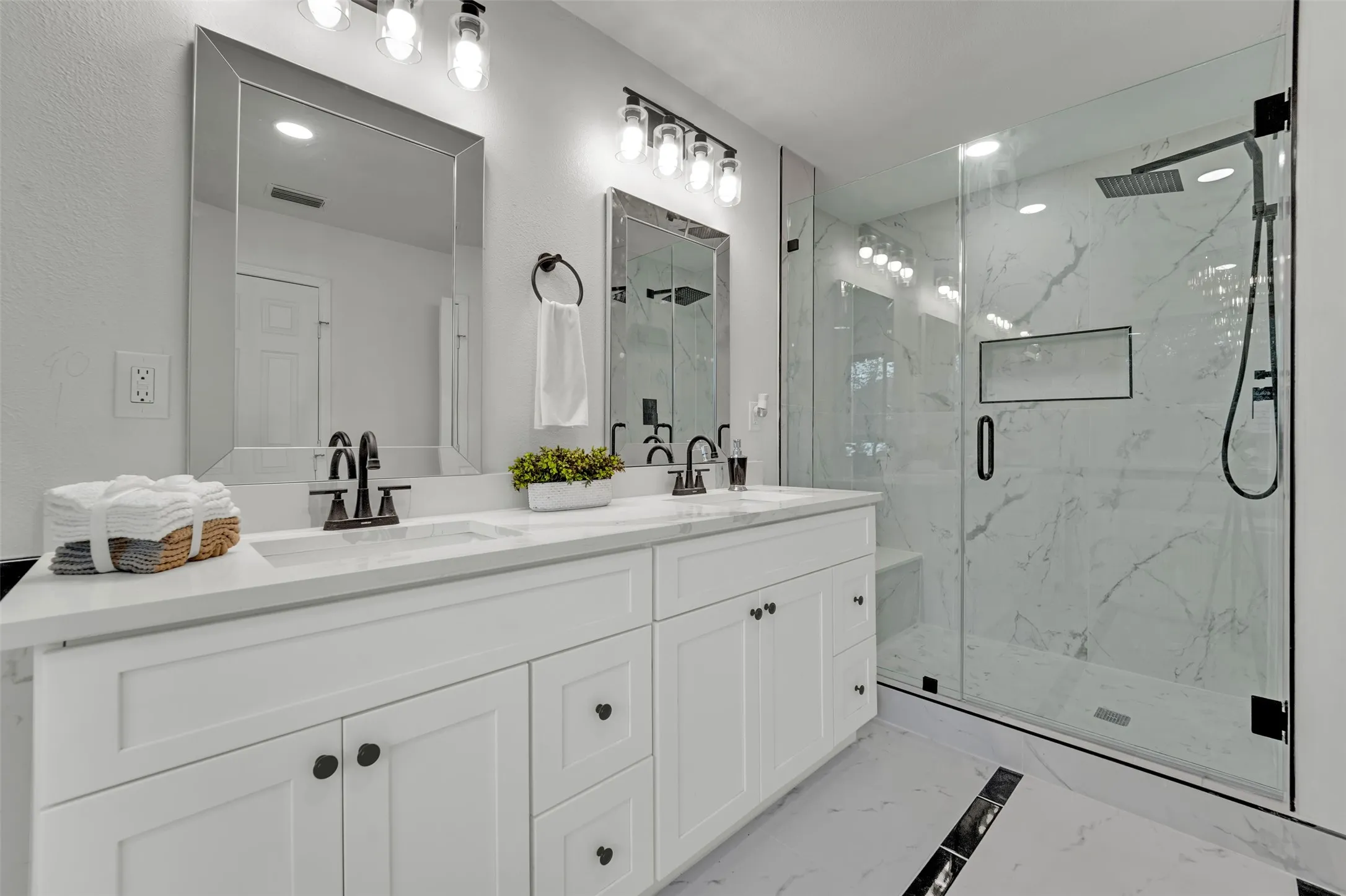 Bathroom with a dual vanity featuring white shaker cabinetry, white countertops, and matte black fixtures