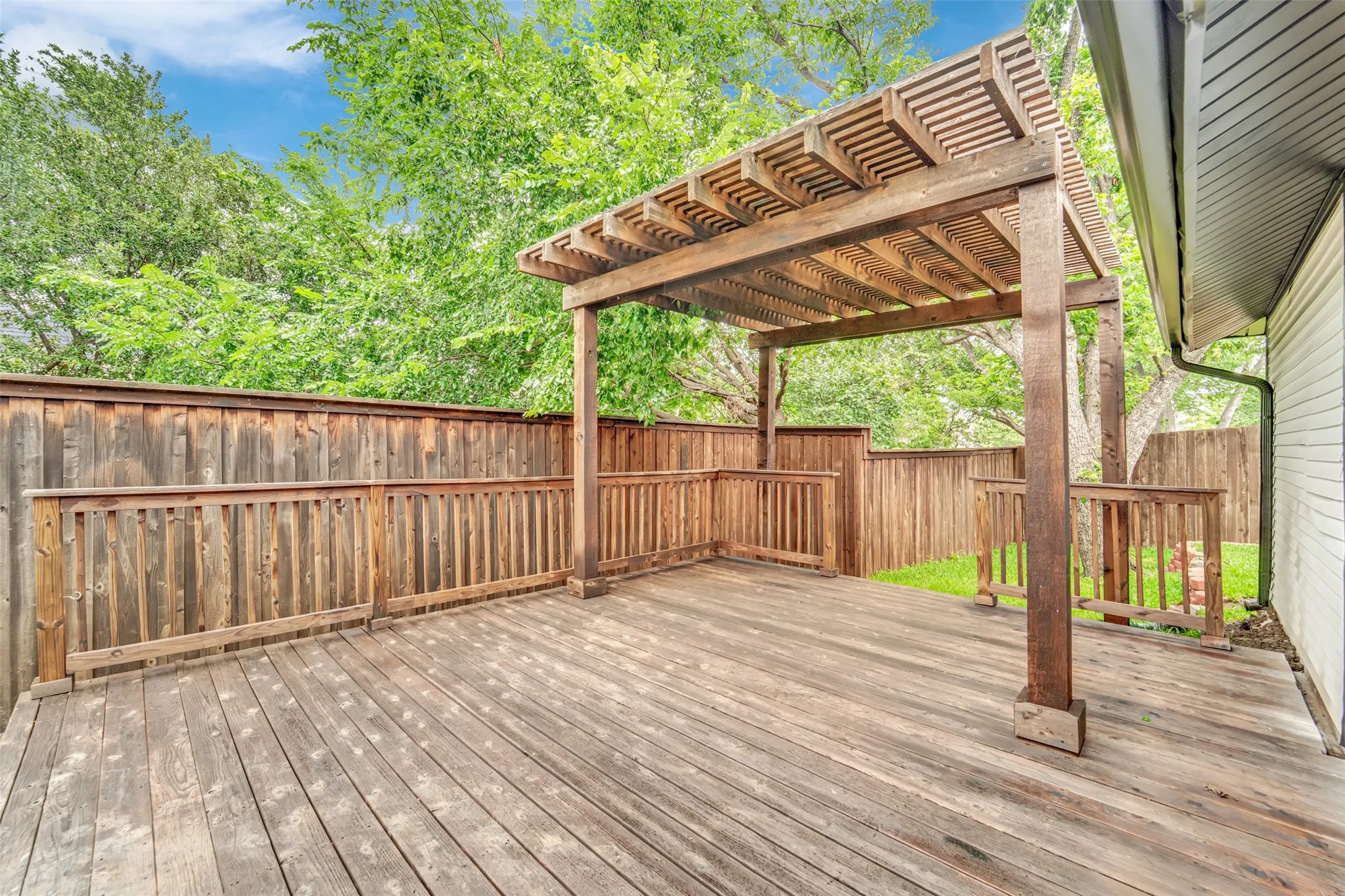 Expansive outdoor deck featuring a wooden pergola, privacy fencing, and perimeter railing