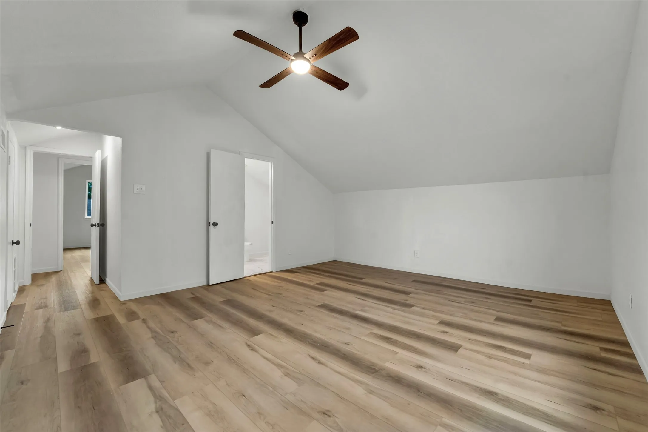 Spacious room featuring wood-finish flooring, a vaulted ceiling, and an integrated ceiling fan with lighting