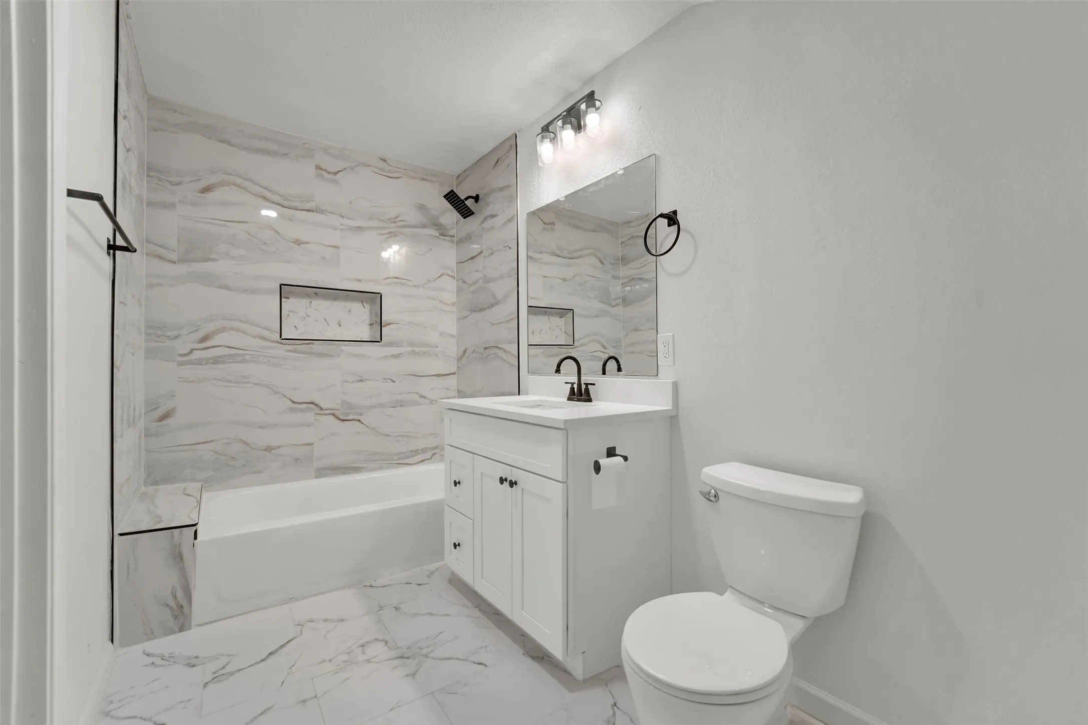 Full bathroom featuring a white vanity with a quartz countertop, a tub-shower combination with large format tiled walls, a matte black shower head, and coordinating matte black fixtures