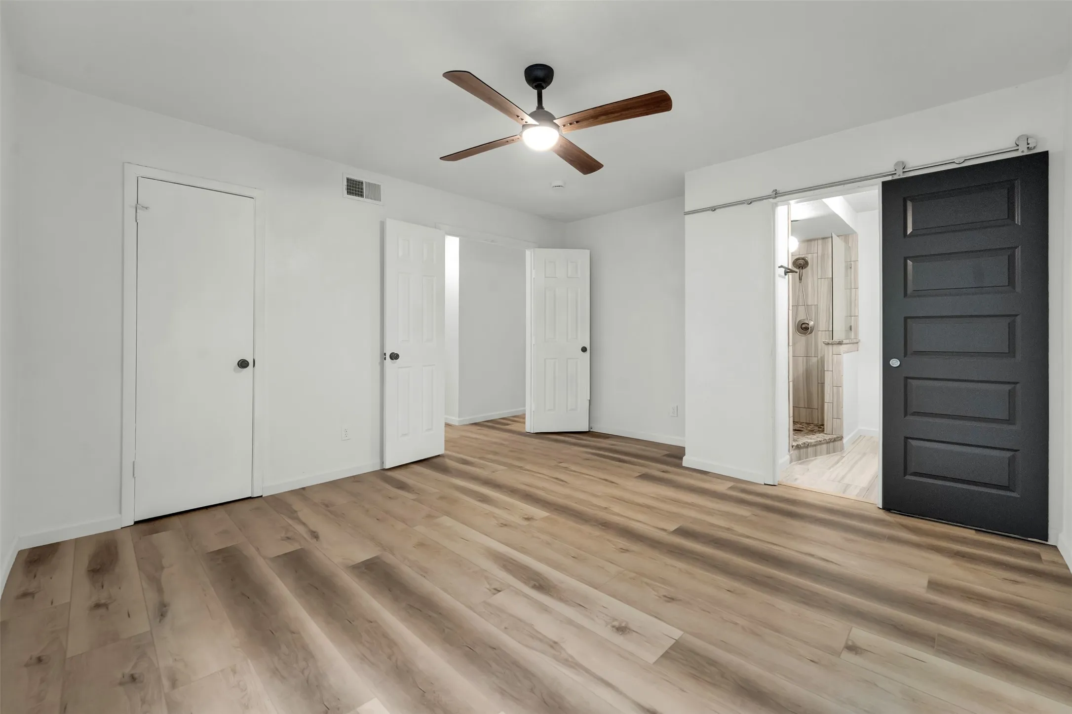 Spacious room featuring wood-finish flooring, a ceiling fan with integrated lighting, and multiple white panel doors