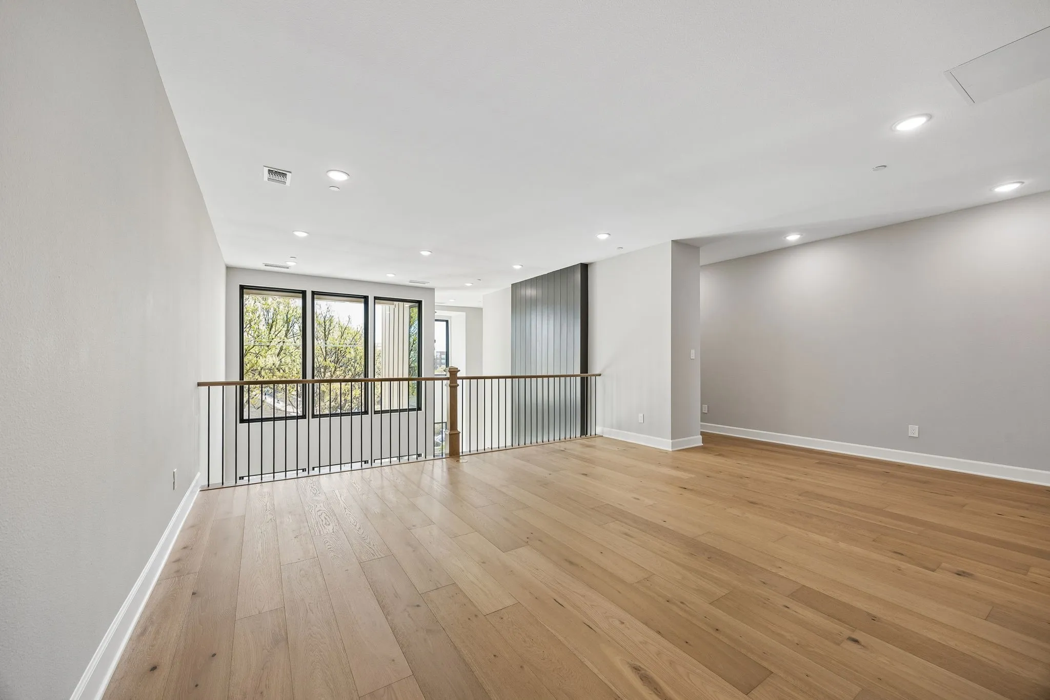 Spacious upper-level area featuring light wood-finish flooring, recessed lighting, and a modern railing with a wood-finish top