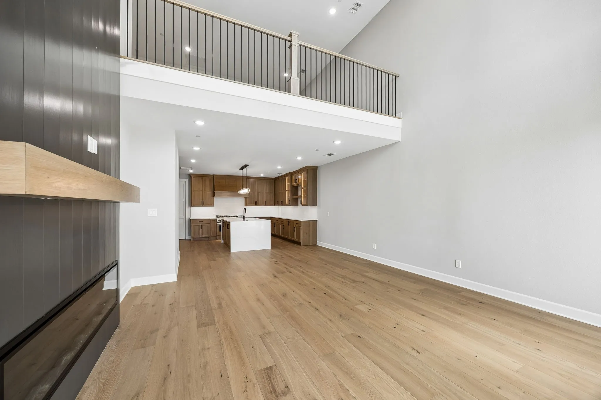 Open-concept main living area with a two-story ceiling, wood-finish flooring, a modern fireplace with a wood mantle, and a kitchen featuring a center island and wood cabinetry