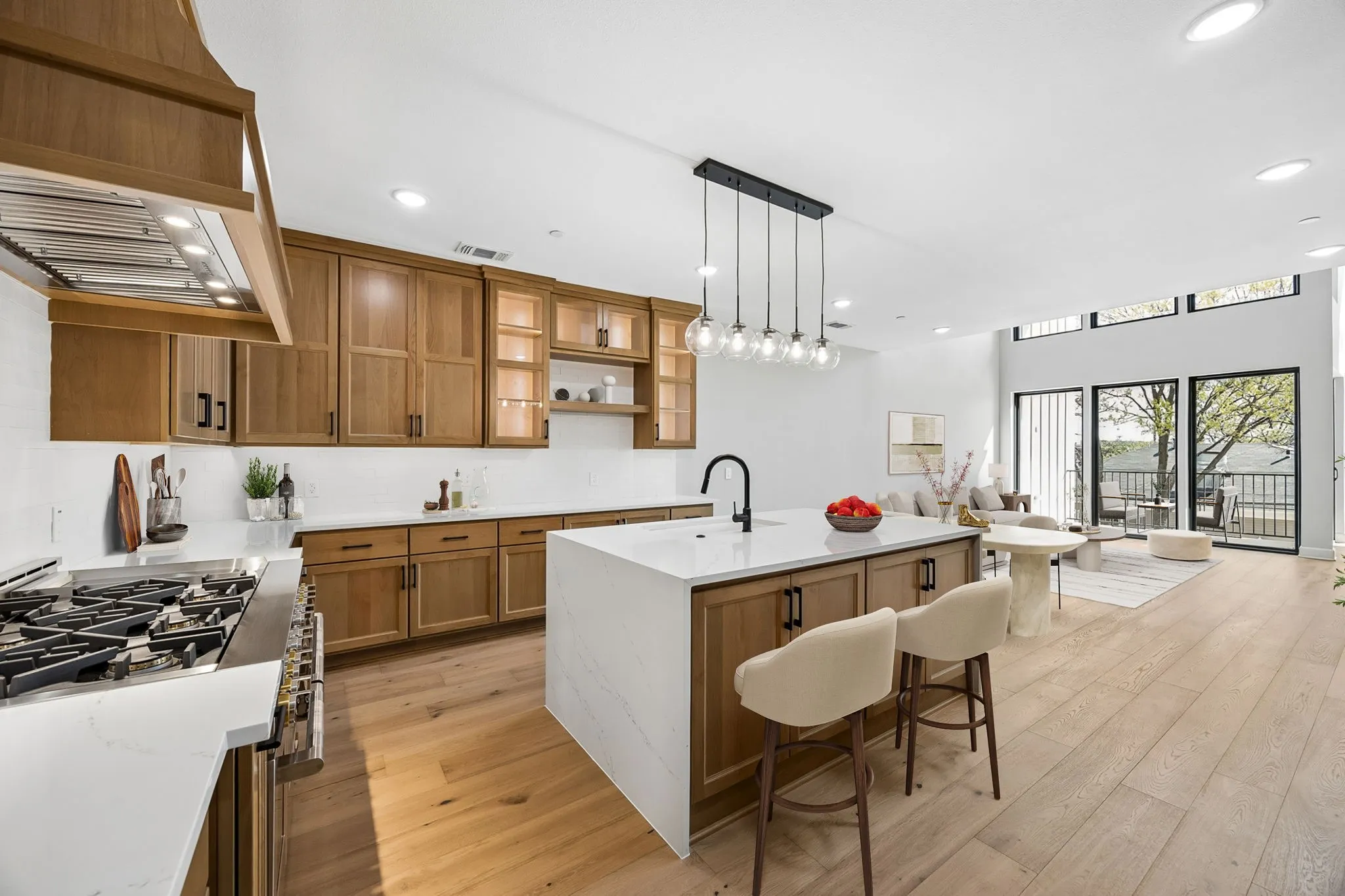 Open-concept living space featuring wood-finish flooring, a kitchen island with seating, integrated appliances, and a wall of glass doors with transom windows