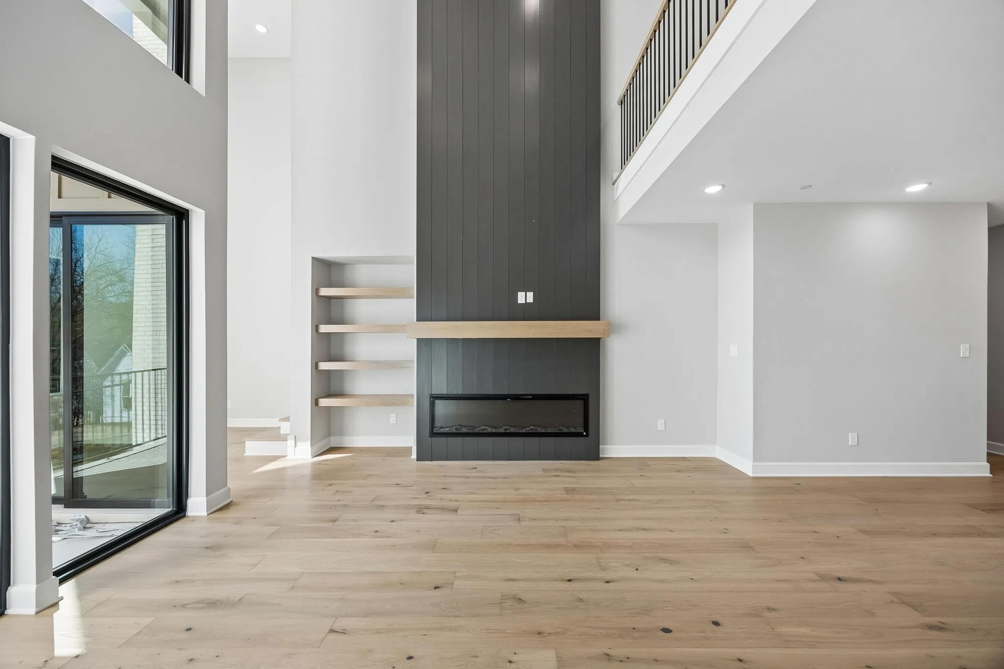 Living area featuring a floor-to-ceiling accent wall with a linear electric fireplace, wood-finish mantel, and integrated shelving