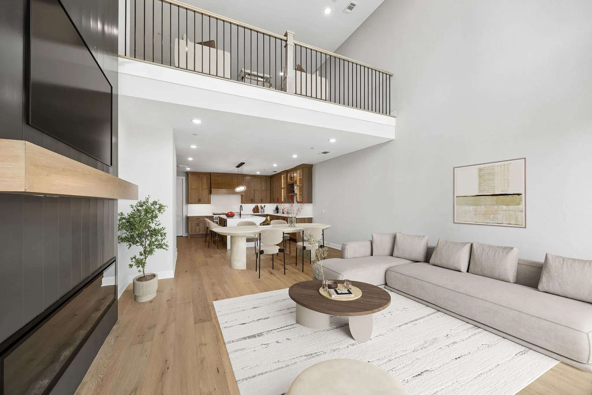 Open-concept living area featuring high ceilings, wood-finish flooring, a contemporary fireplace with a wood mantle, and a second-story loft with an iron railing