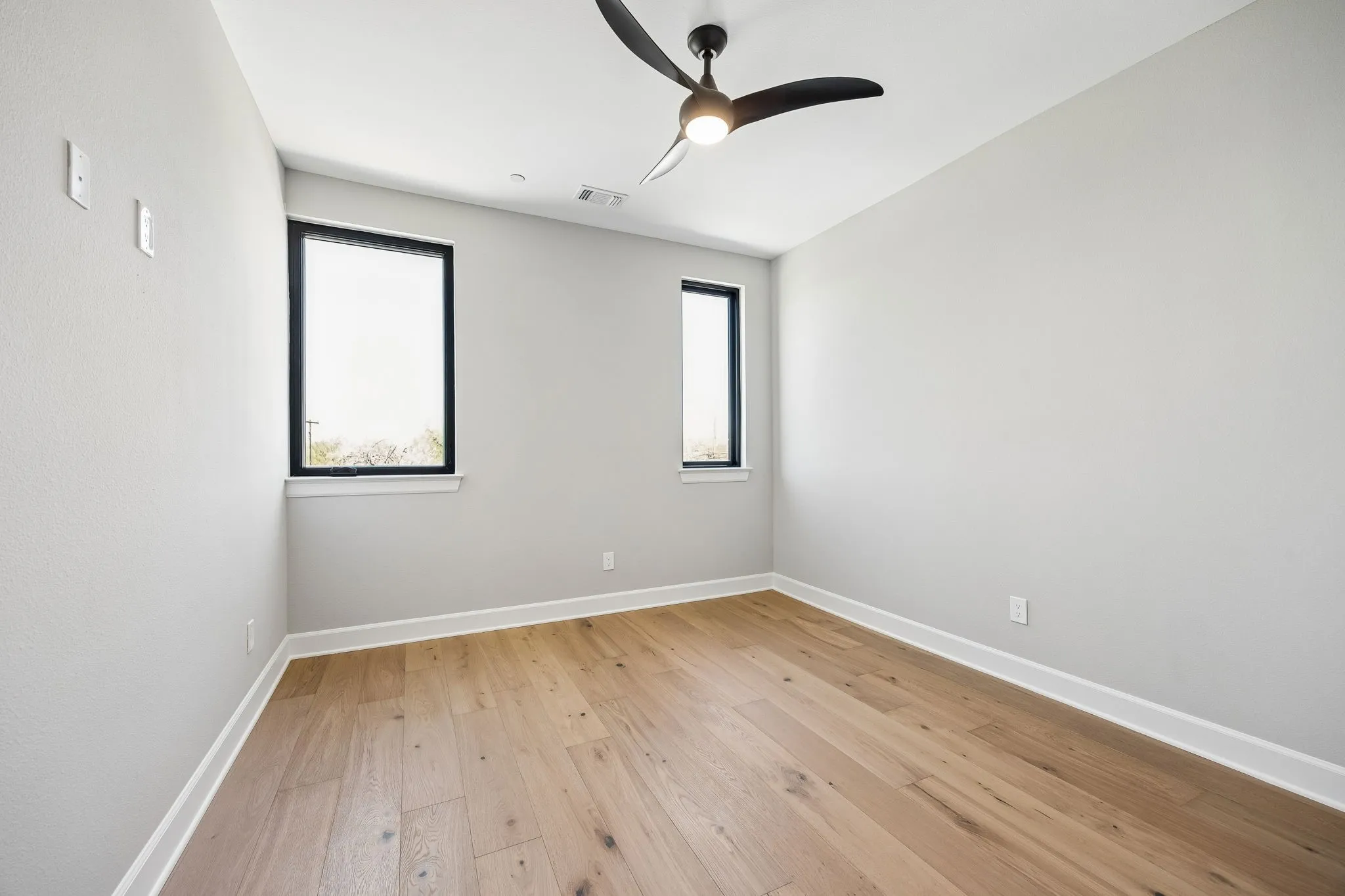 Spacious room featuring light wood-finish flooring, white baseboards, and a contemporary ceiling fan with integrated lighting