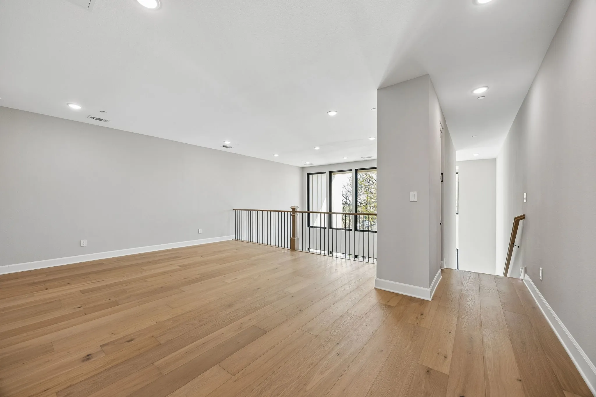 Open-concept landing with wood-finish flooring, recessed lighting, and a modern black metal railing