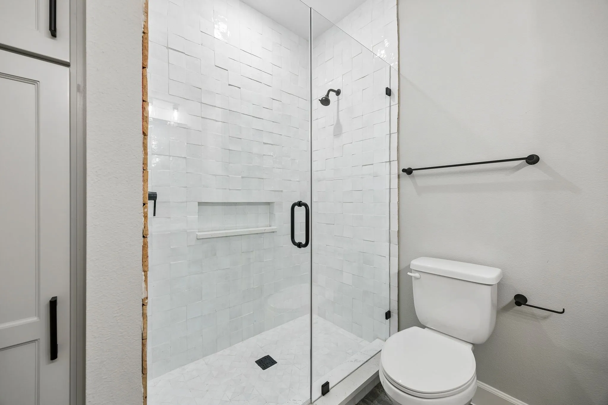 Glass-enclosed shower featuring white subway tile, a recessed shower niche, and matte black fixtures