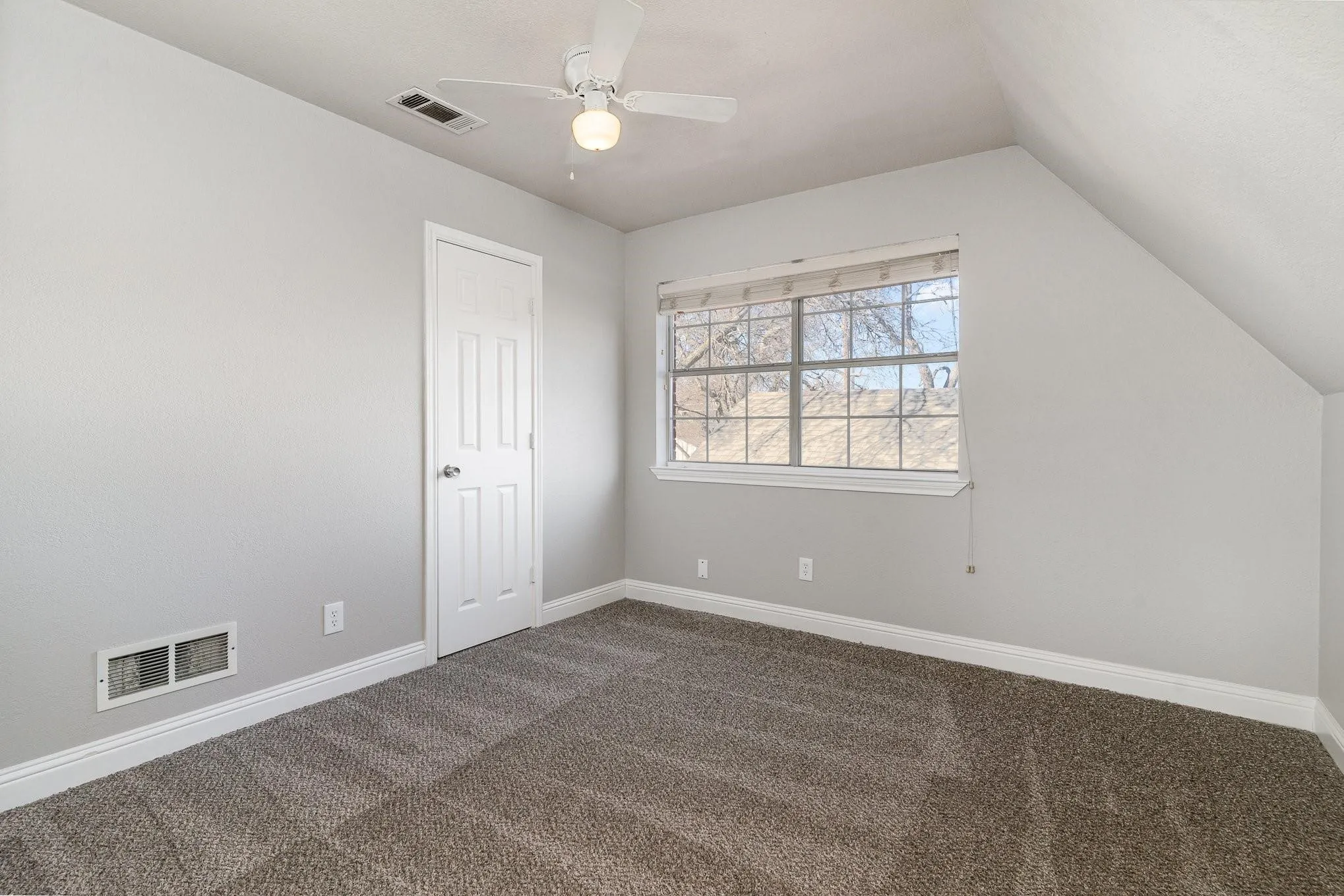Room featuring neutral gray wall paint, textured carpeting, a multi-pane window with blinds, and an angled ceiling
