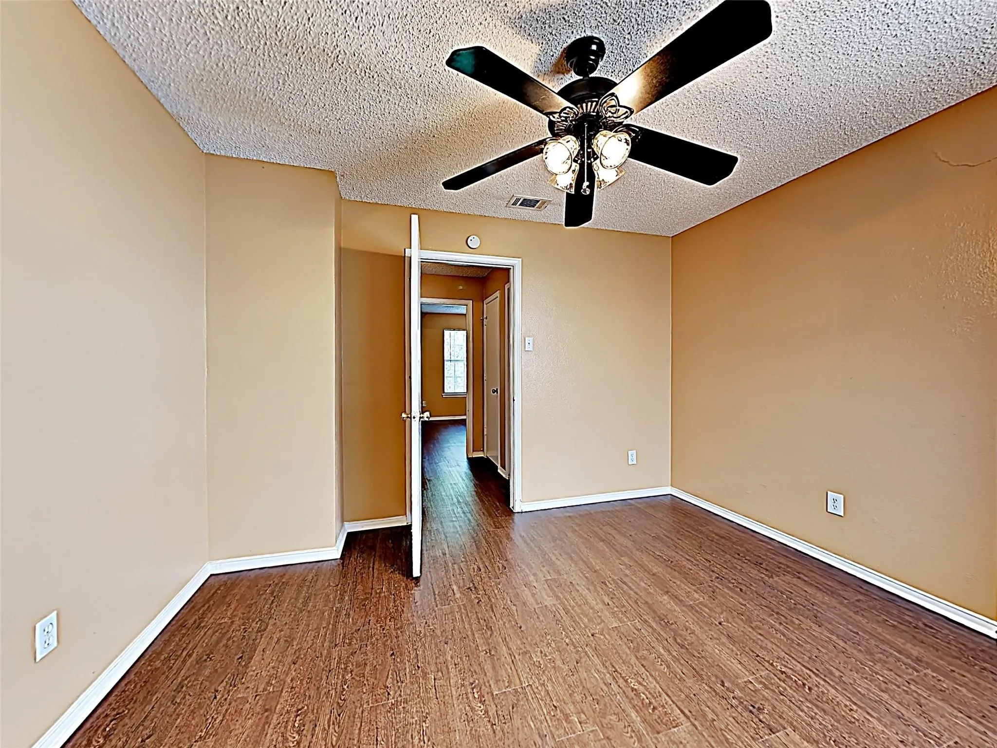 Warm-toned walls complement wood-finish flooring in this room featuring a ceiling fan with integrated lighting