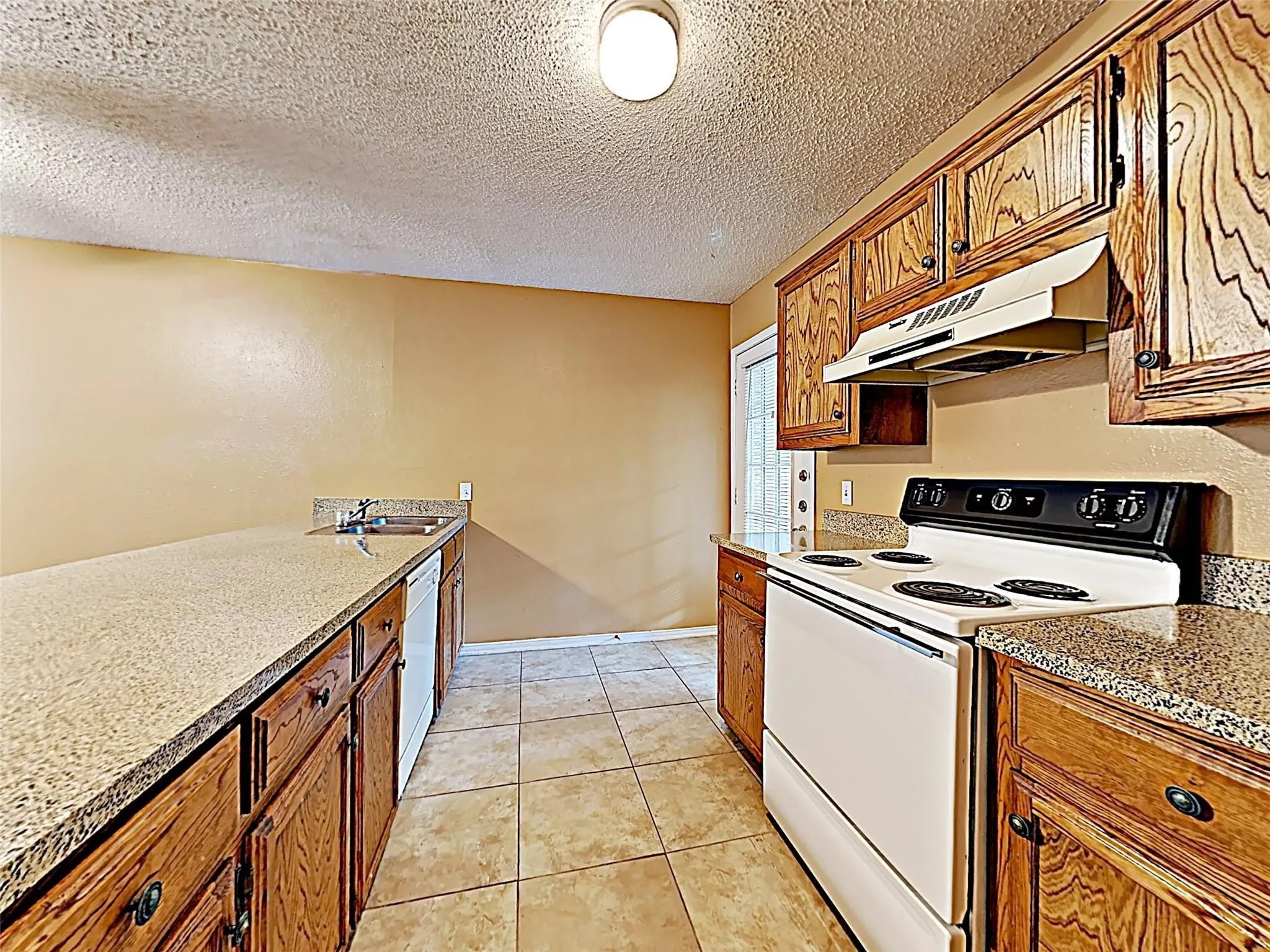 Kitchen featuring wood cabinetry, light-toned countertops, tile flooring, and white appliances