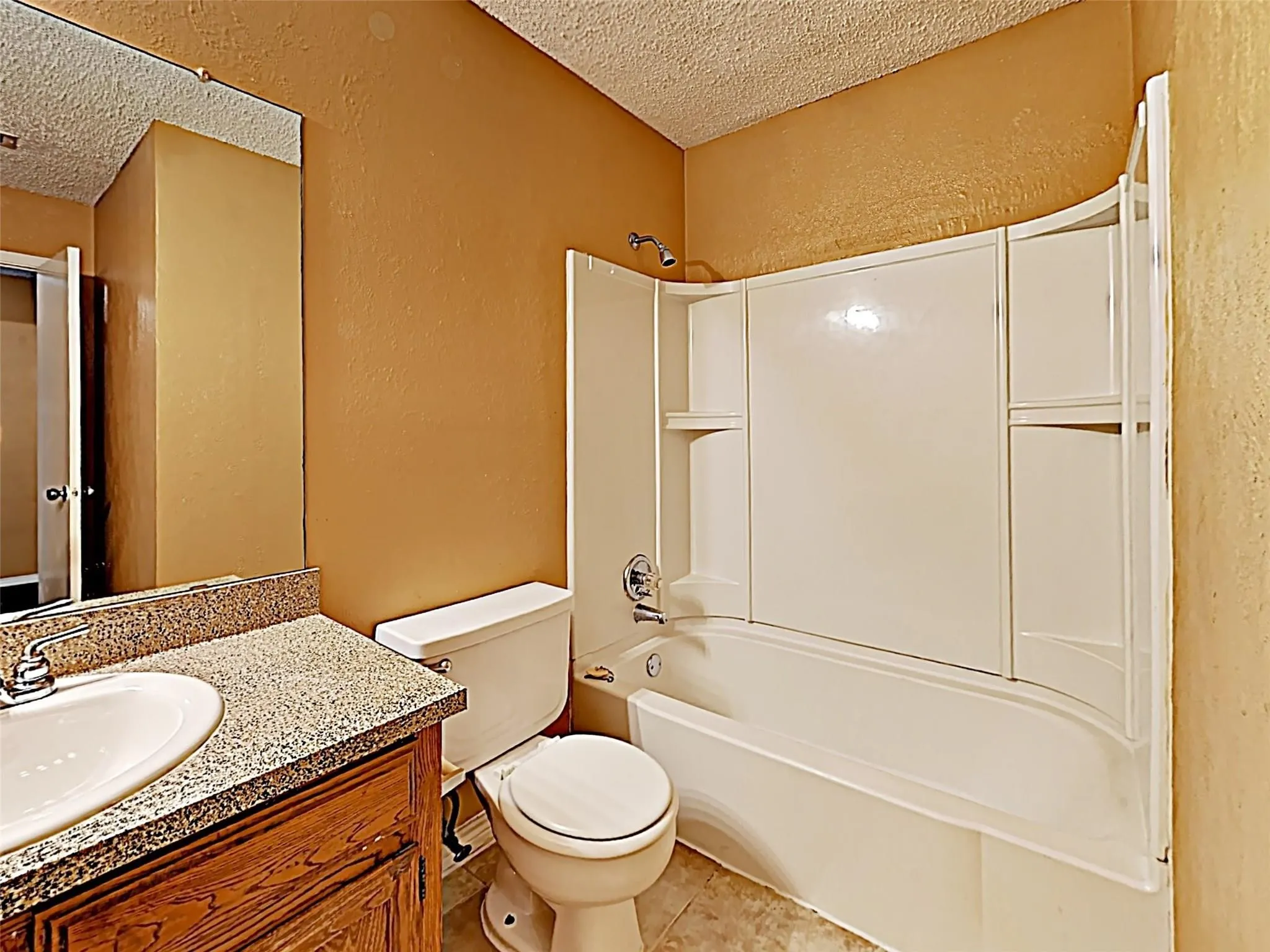 Bathroom featuring a built-in tub with a shower fixture, a vanity with a white basin sink and a stone-look countertop, and a wall-mounted mirror