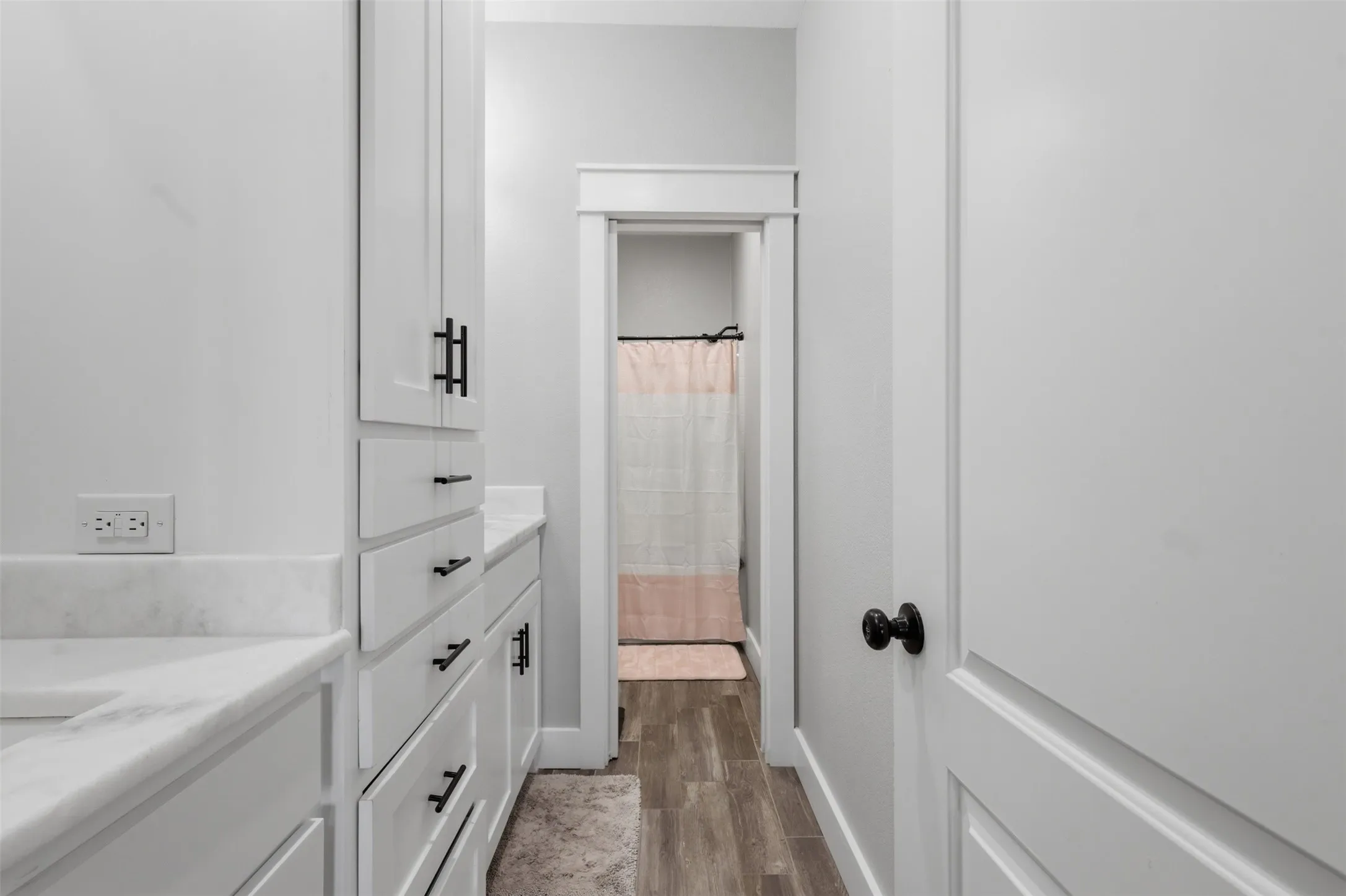 Bathroom featuring white cabinetry with matte black hardware, white countertops, and wood-look flooring