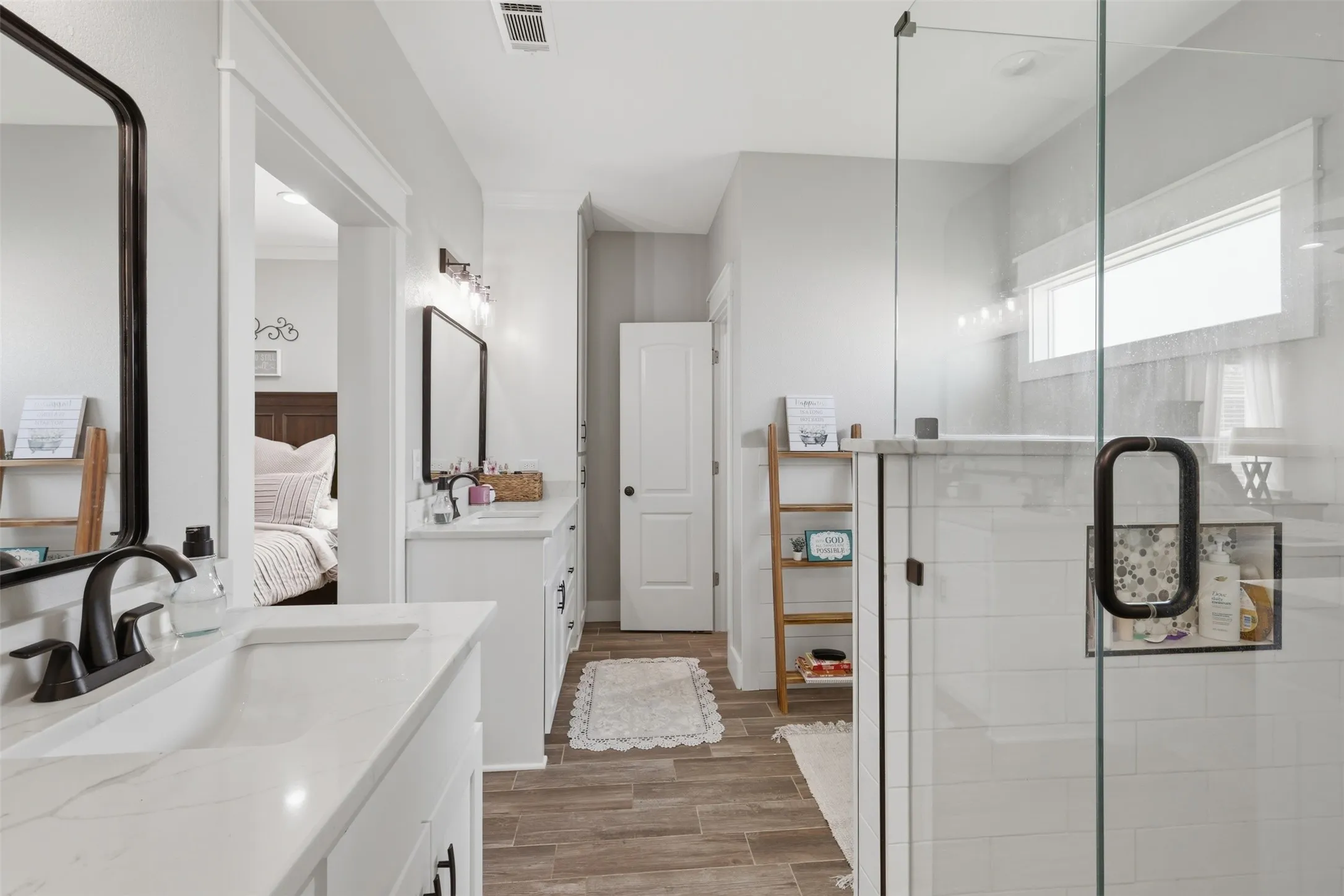 Bathroom featuring a glass-enclosed shower, dual vanity with white countertops, wood-finish flooring, and black fixtures