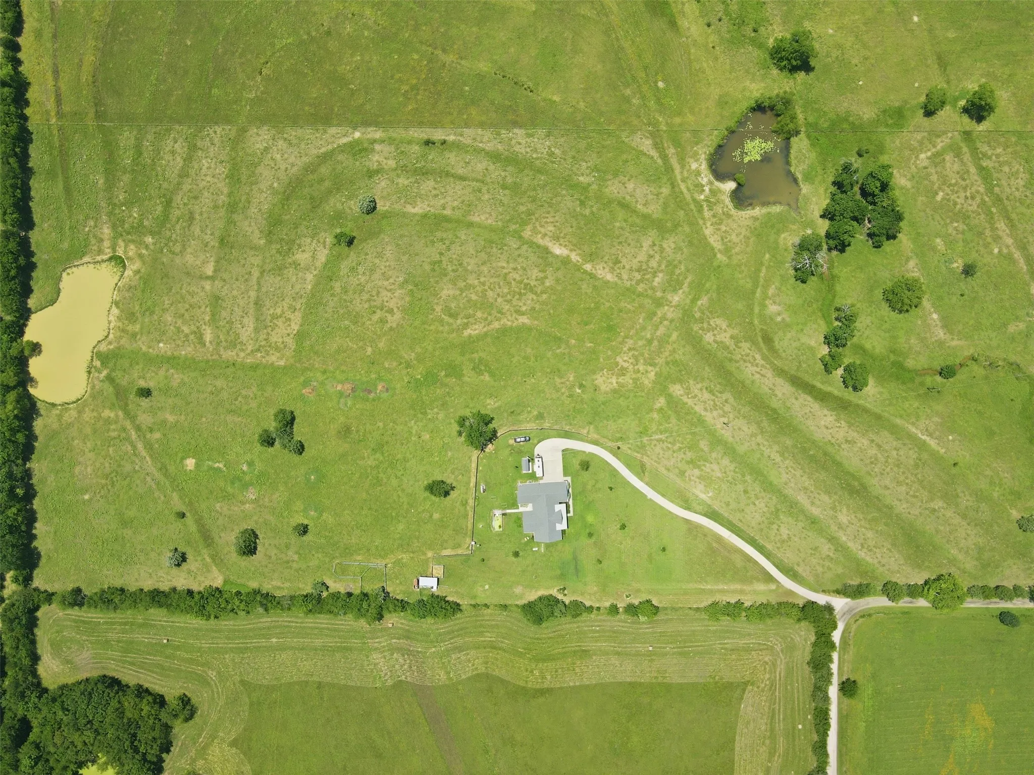 Expansive agricultural property featuring a central residence, a long driveway, two ponds, and mature tree clusters