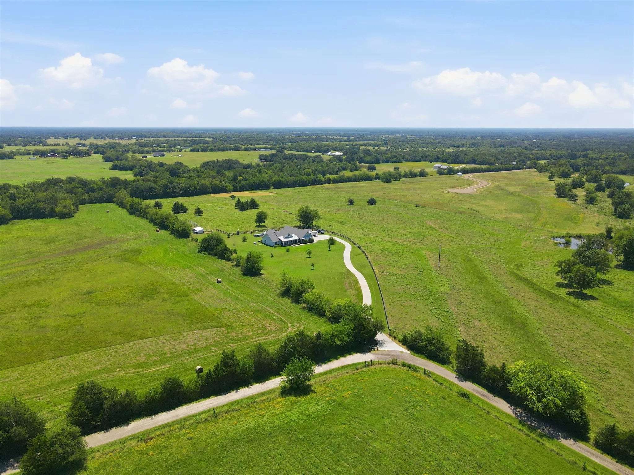 Expansive green acreage featuring a single-story residence, a paved circular driveway, multiple mature trees, and a pond