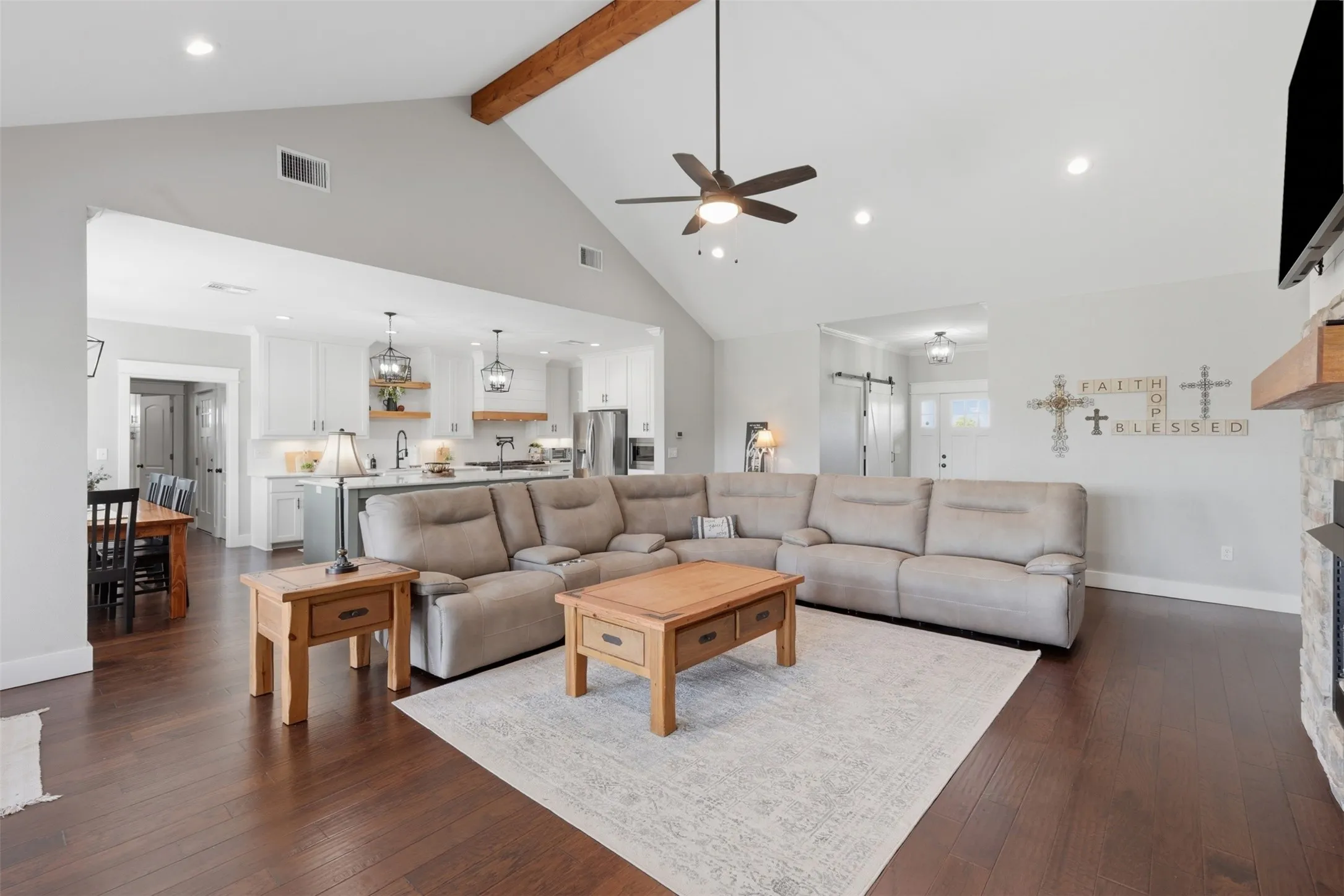 Spacious living area featuring wood-finish flooring, a vaulted ceiling with exposed wood beam, and recessed lighting