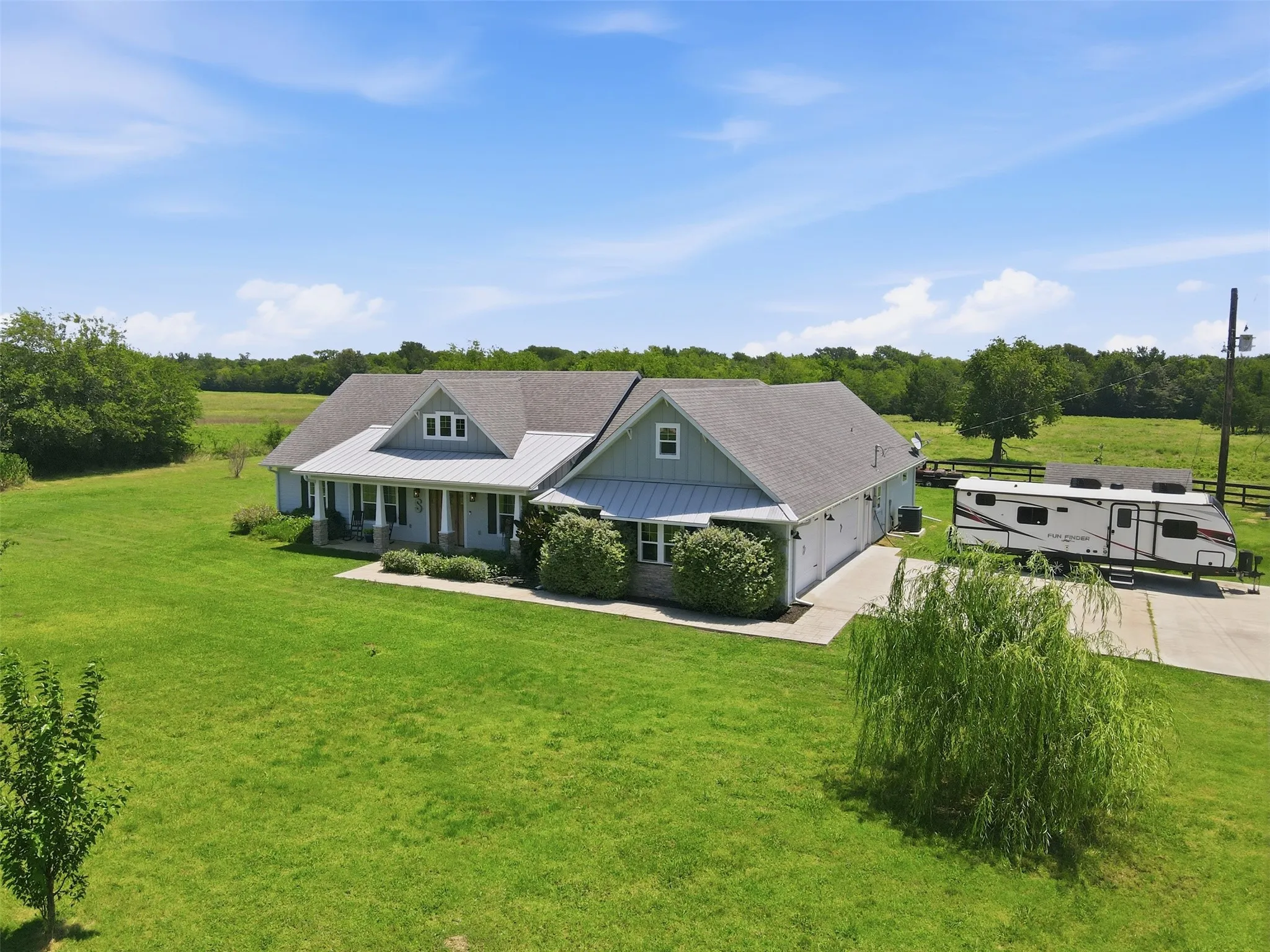 Expansive property featuring a single-story residence with a covered front porch, an attached multi-car garage, and a long concrete driveway