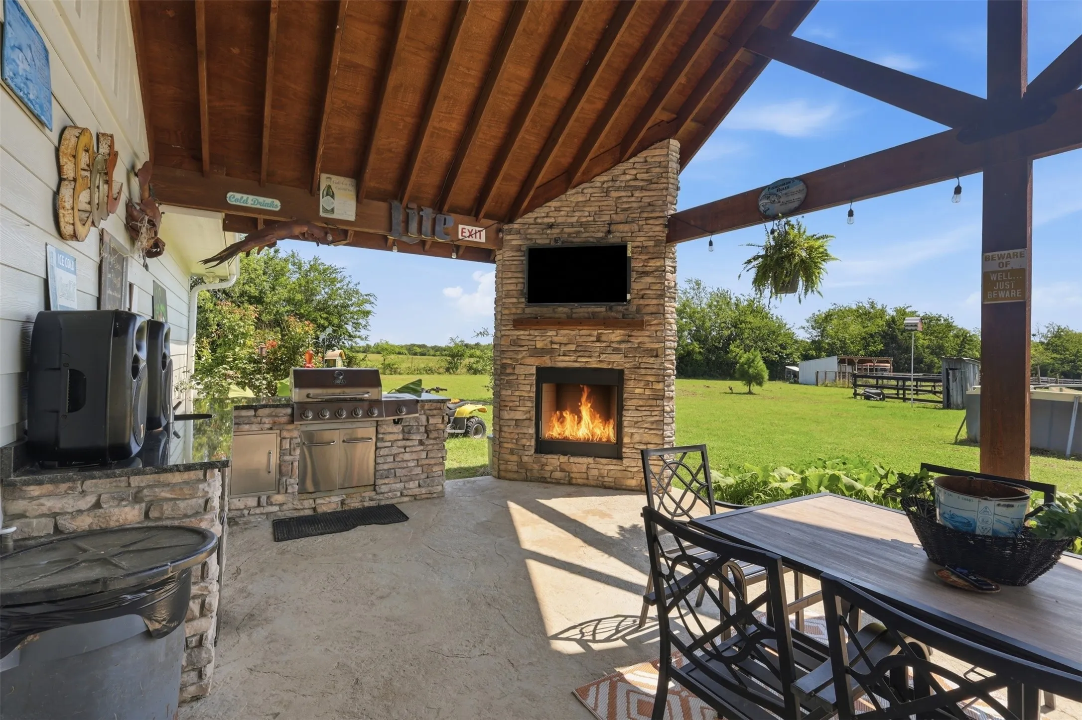 Covered outdoor living space featuring a stone-clad fireplace with a mounted television