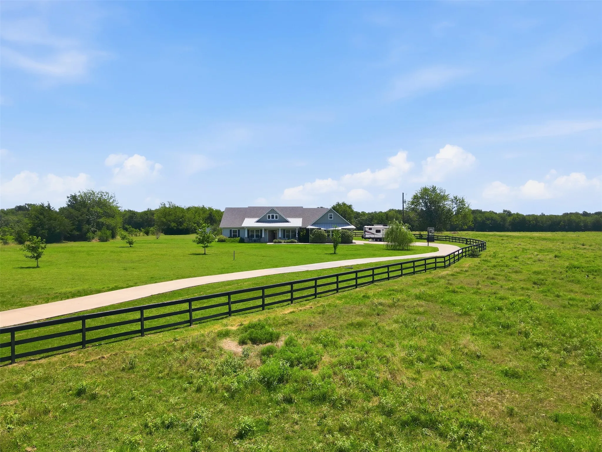 Expansive green acreage featuring a meandering paved driveway and a black multi-rail fence