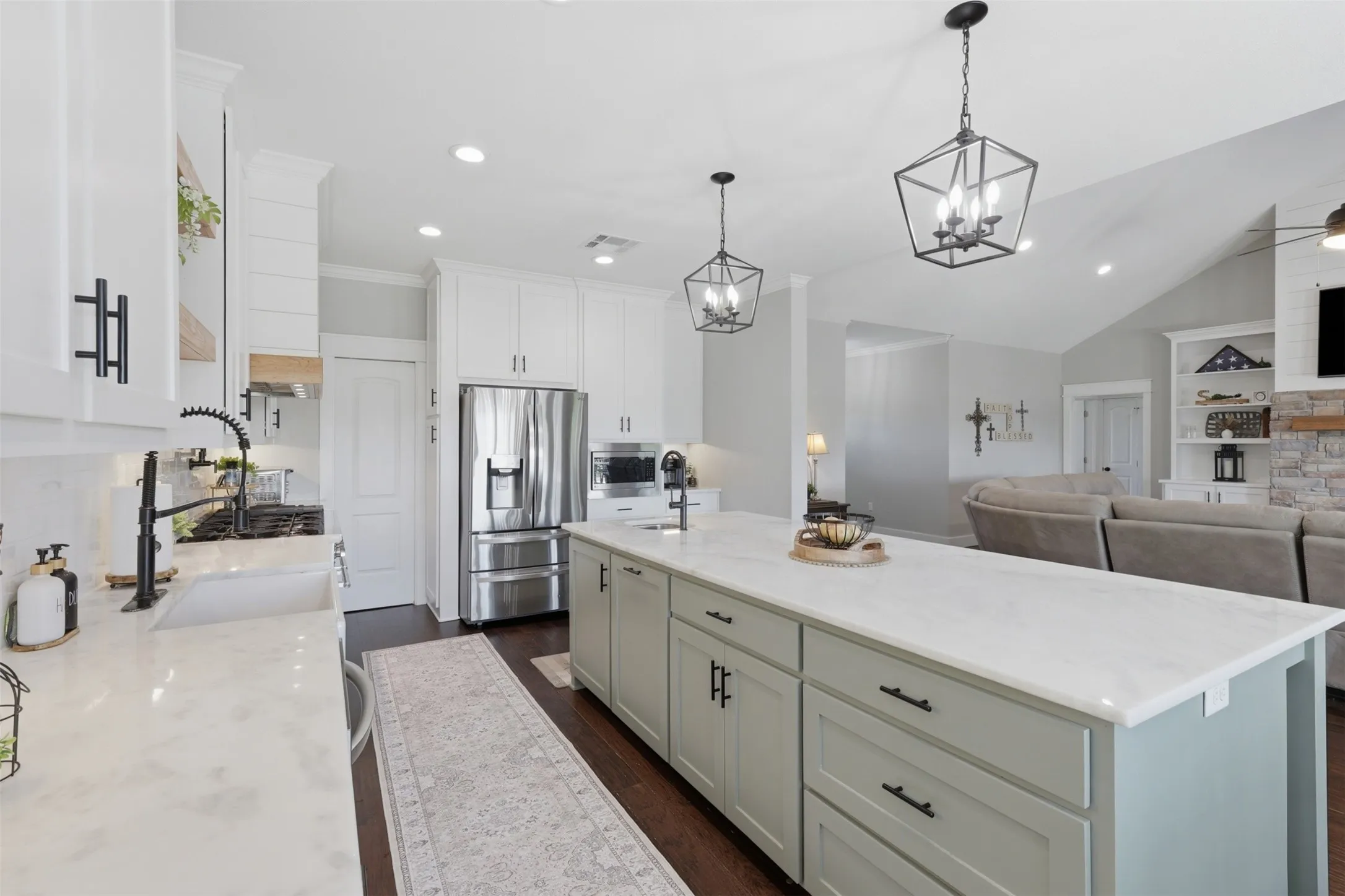 Gourmet kitchen featuring a large central island with light-toned countertop, recessed lighting, stainless steel appliances, white cabinetry with black hardware, and dark wood-finish flooring