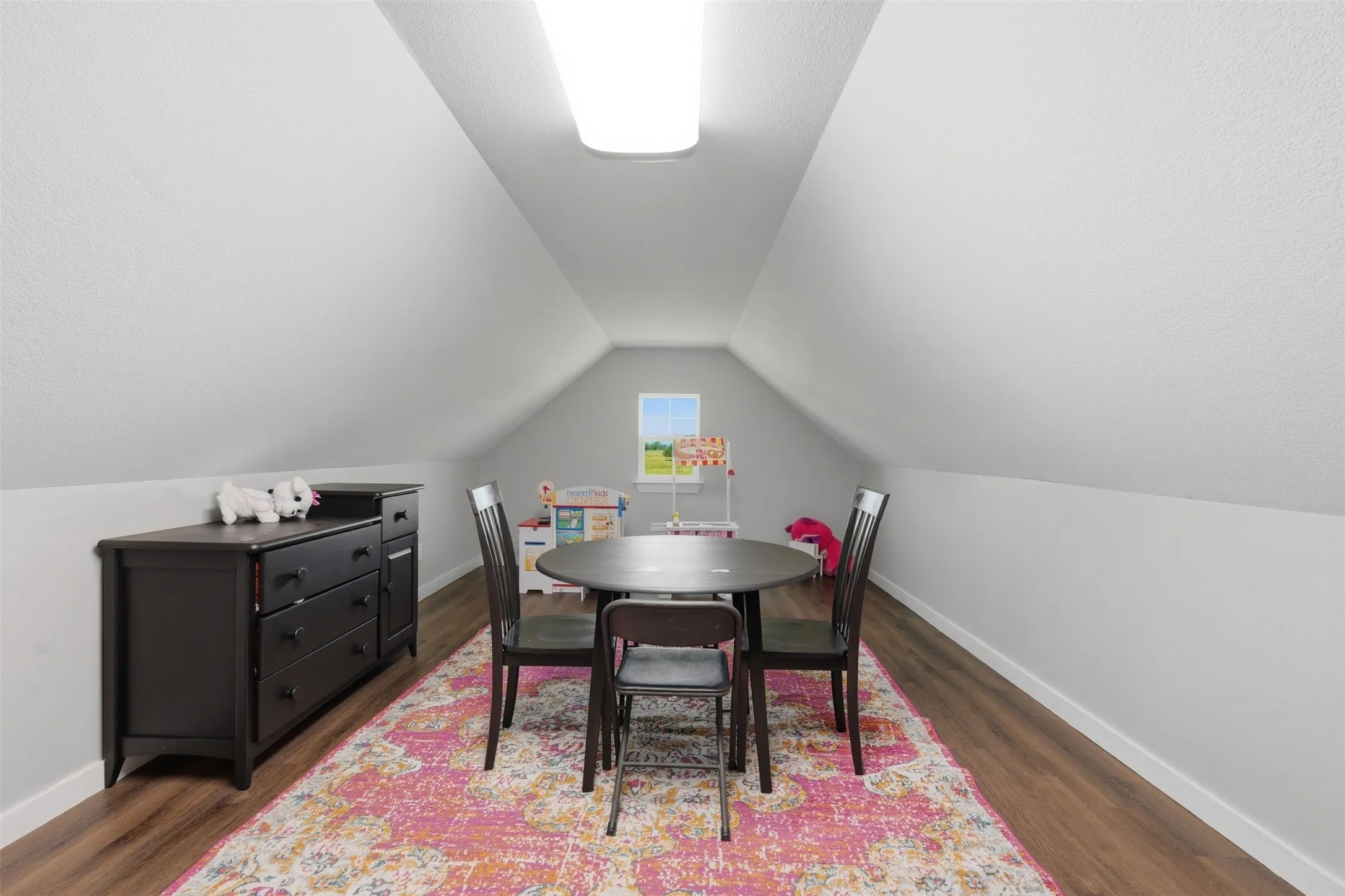 Versatile attic space featuring sloped ceilings, wood-finish flooring, a rectangular window, and a flush-mount ceiling light