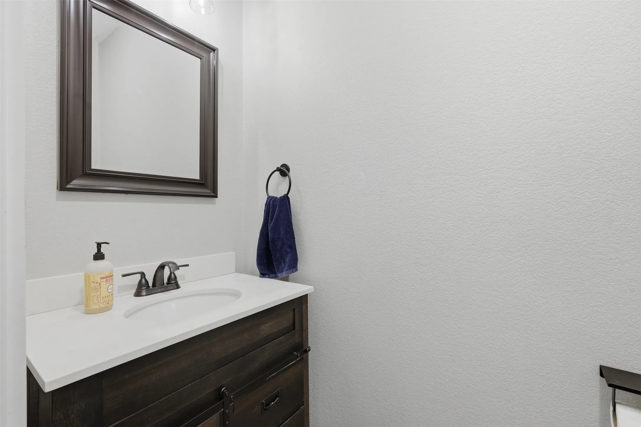 Bathroom vanity featuring a dark wood-finish cabinet with barn-door style hardware, white countertop with an integrated sink, and dark bronze faucet