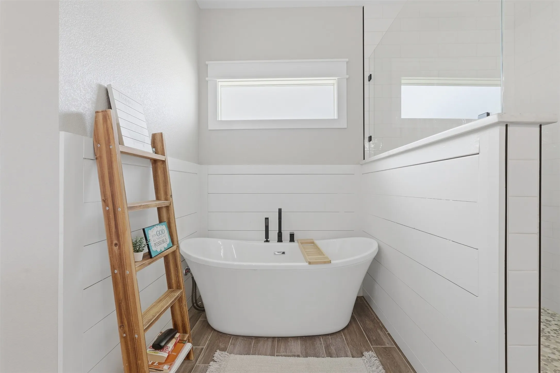 Freestanding soaking tub with black fixtures, set against white shiplap wall paneling