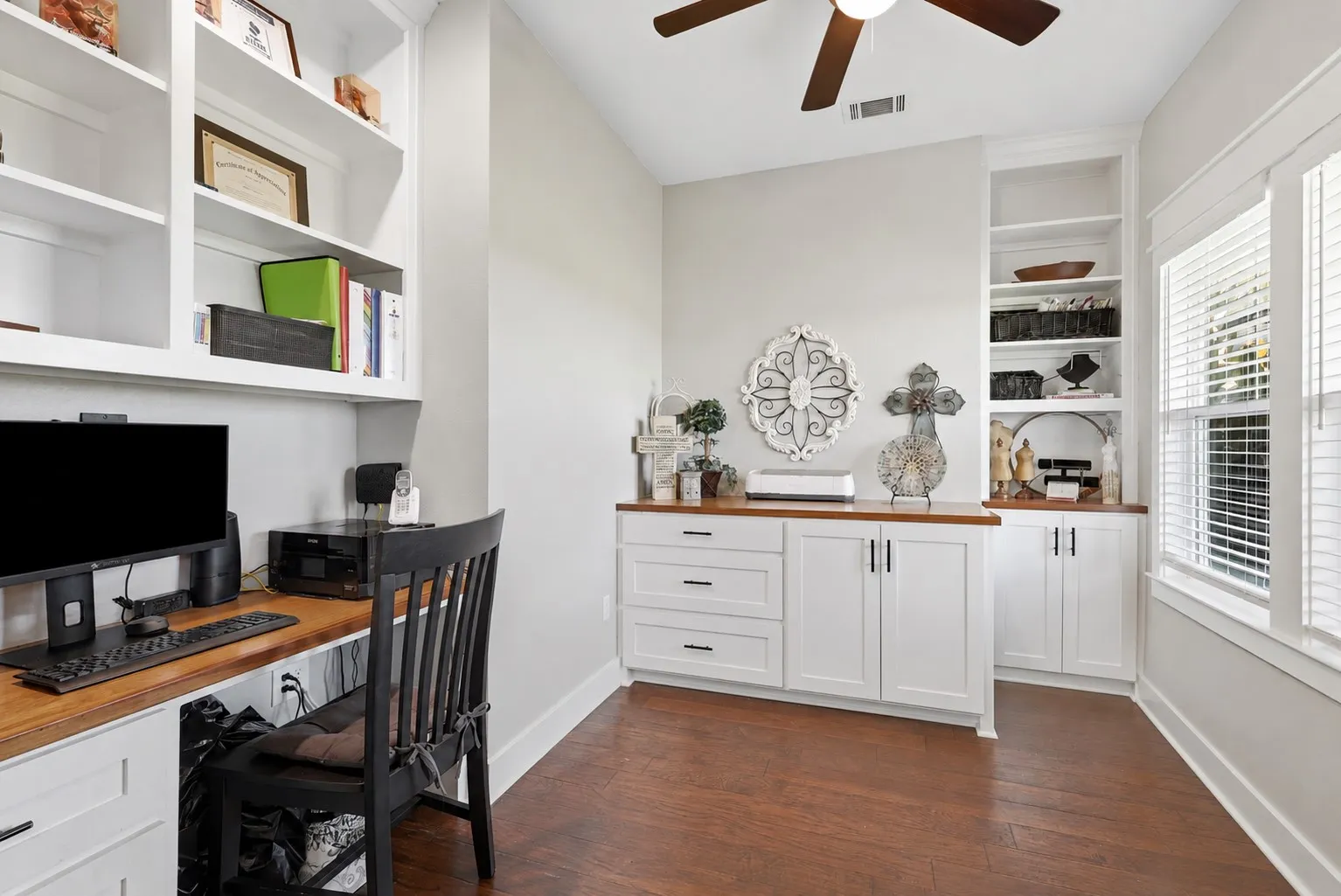 Dedicated office space featuring extensive built-in cabinetry, wood-finish flooring, and a ceiling fan