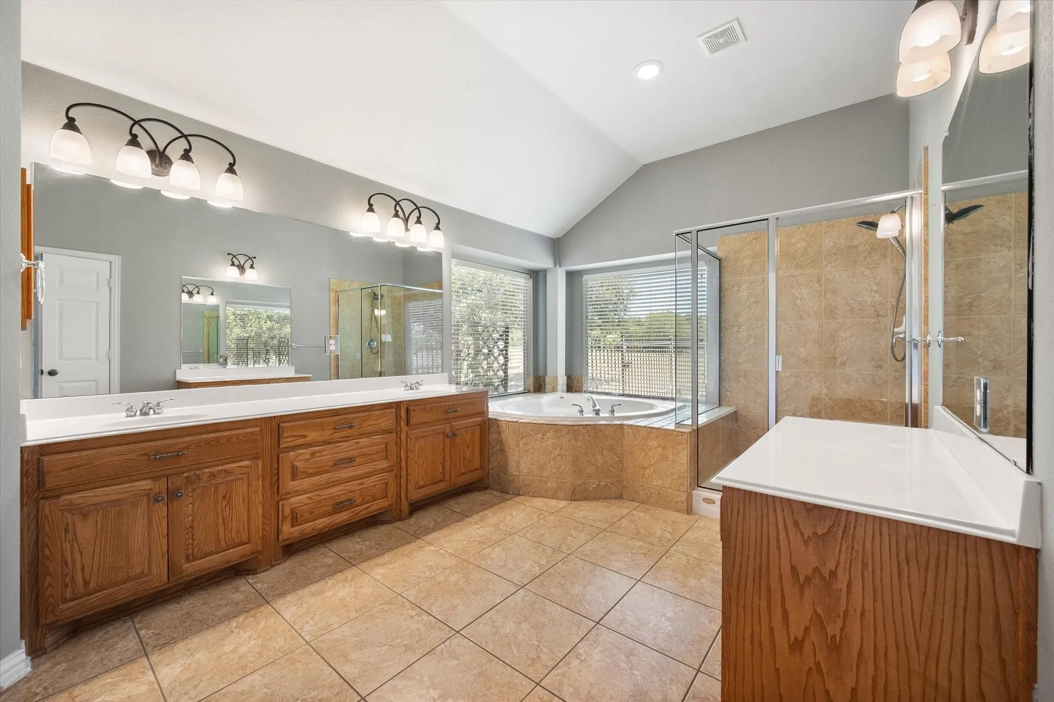 Spacious primary bath features dual vanities, garden tub, separate shower, and warm tile finishes.