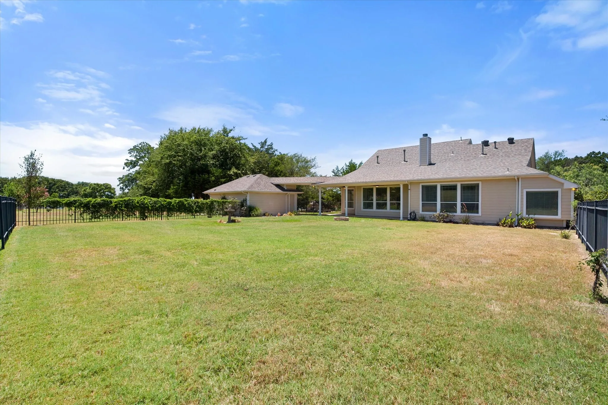 Rear exterior view shows the covered porch, spacious fenced backyard, and private country setting.