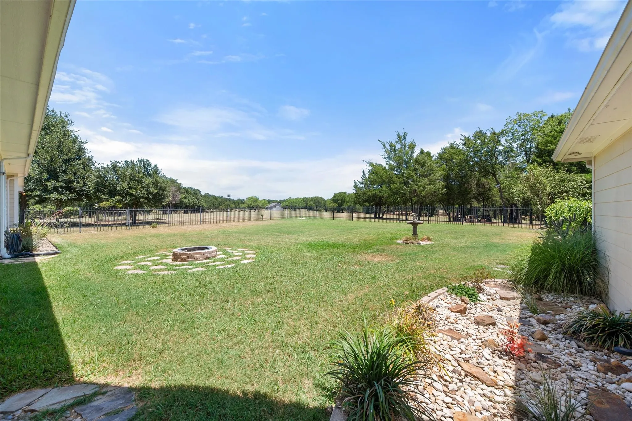 Fenced backyard includes open grass, native landscaping, and a fire pit area for outdoor gatherings.