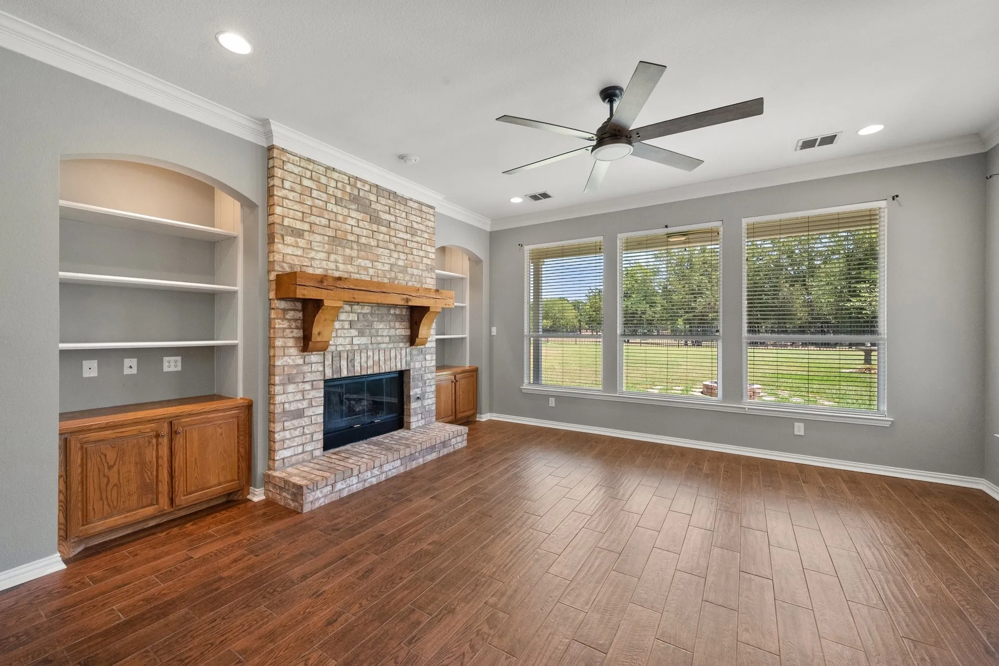 Living room features a brick fireplace, built-in cabinets, ceiling fan, and large backyard-facing windows.