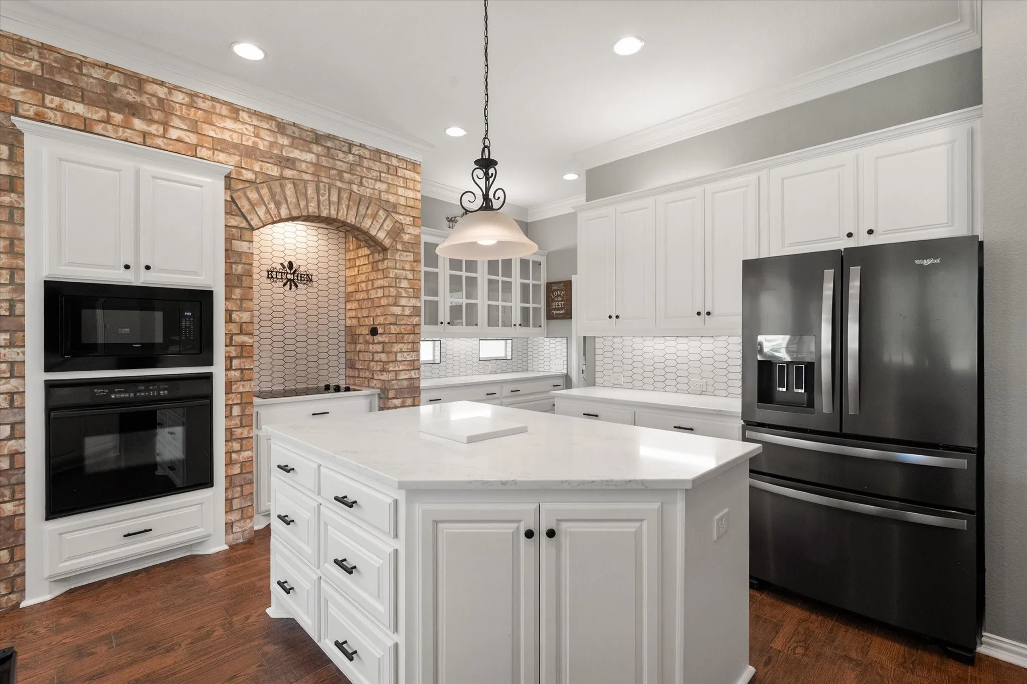 Spacious kitchen includes a large island, white cabinets, granite countertops, and black appliances.