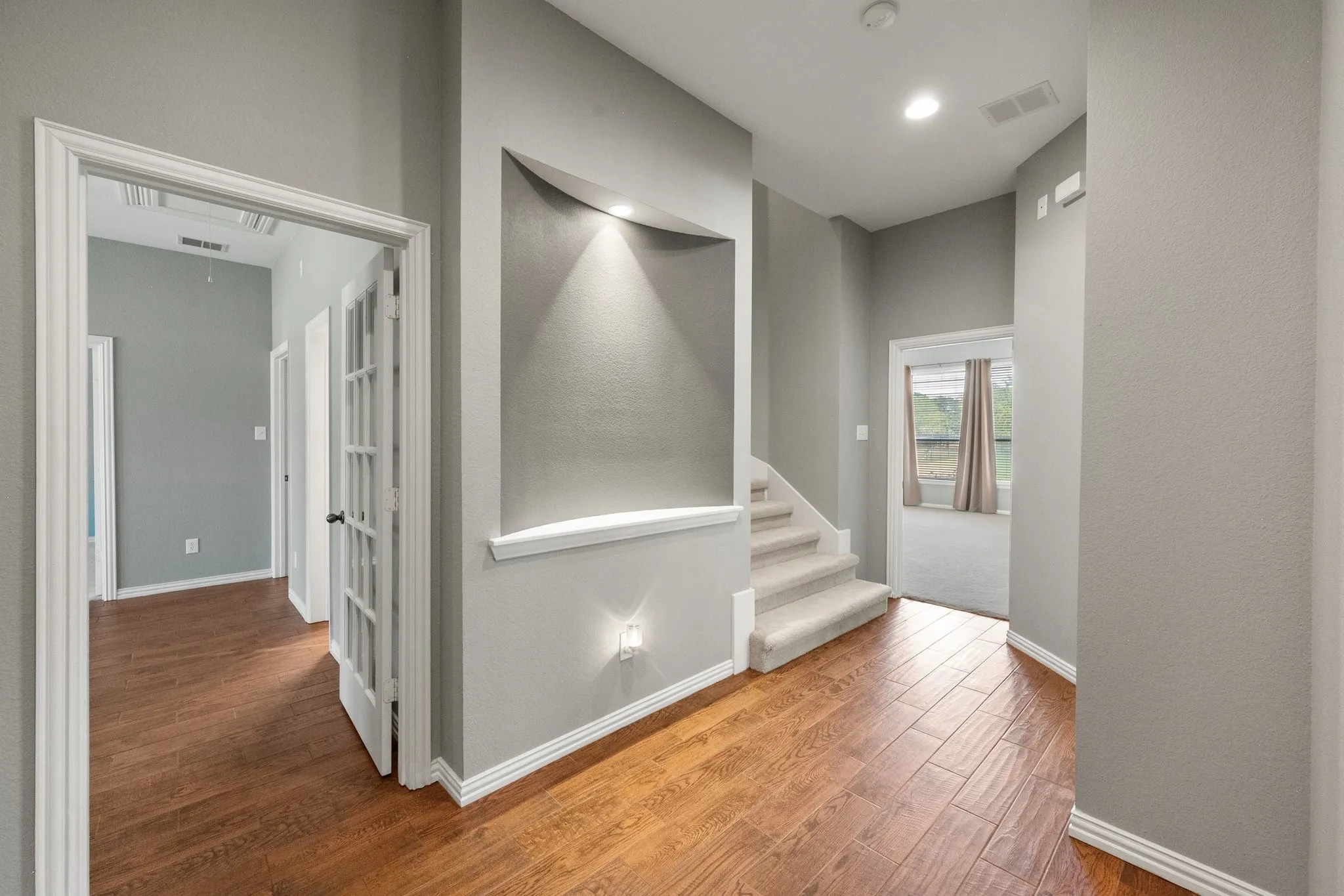 Hallway view highlights the home’s staircase niche, and warm wood-look flooring.