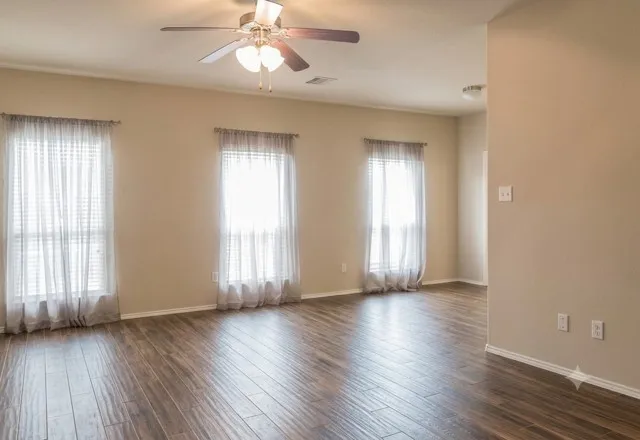 Spacious interior room featuring wood-finish flooring, light tan walls, and multiple windows
